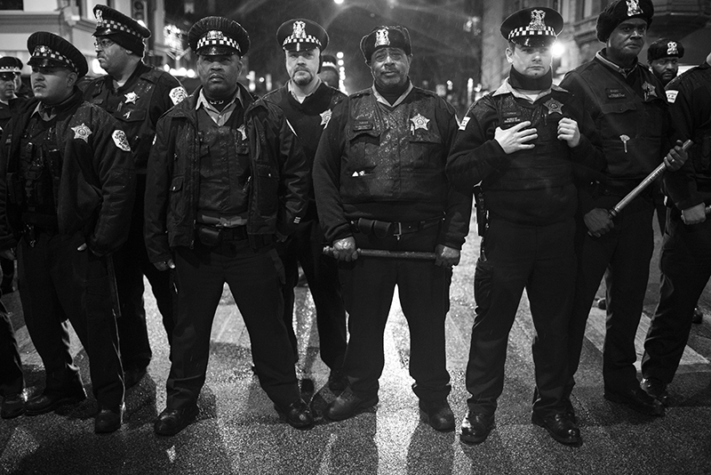 Chicago police officers line up and block protestors from going North during one of the many moments in the Laquan McDonald protests. Hundreds of people protested the police killing of 17 year old Laquan McDonald at the hands of Chicago police officer Jason Van Dyke. McDonald was shot sixteen times and the video was withheld from public view until a judge ordred it released. McDonald was holding a small knife but was shot repeatedly in the dashcam video. The family was paid 5 million dollars in a settlement with the City of Chicago, but yesterday officer Van Dyke was also charged with murder after a whistleblower brought the video to the attention of a local journalist who then sued the city to have it released. The City of Chicago's Police Department has a long and difficult history associated with police brutality reaching back decades.