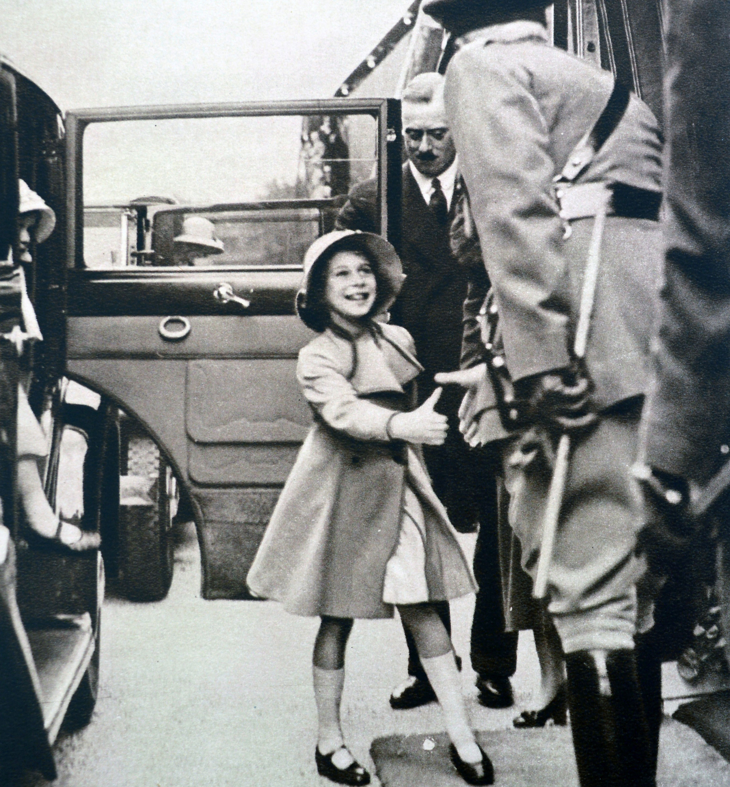The Duchess of York took the children to see a daylight dress rehearsal of the Aldershot Tattoo. Here Princess Elizabeth greets the officer of the guard while Princess Margaret alights from the car at Rushmoor Arena. January 1935.