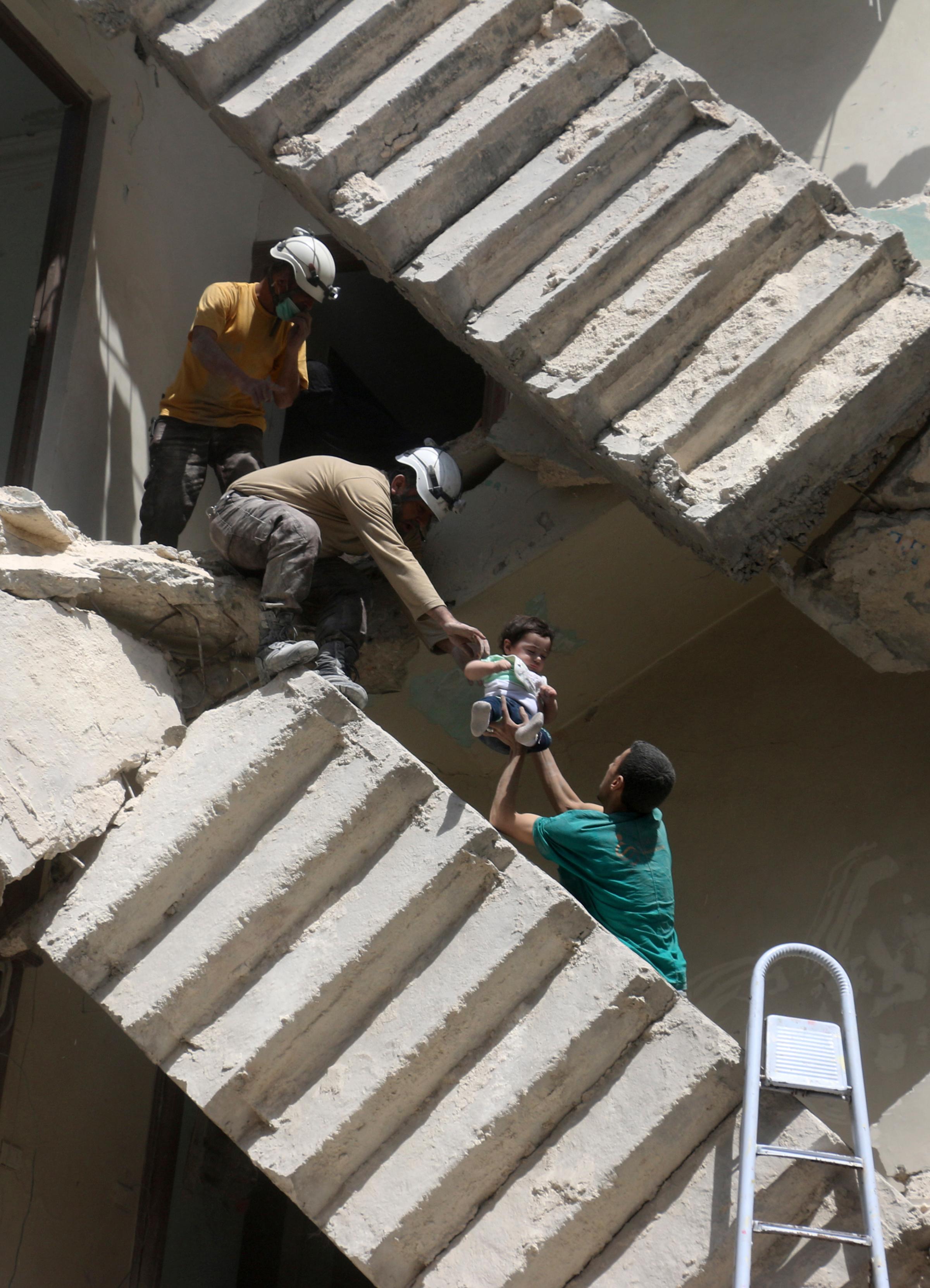 Civil defense volunteers help evacuate a child from a destroyed building following a reported airstrike on a rebel-held neighborhood in Aleppo, Syria, April 28, 2016.