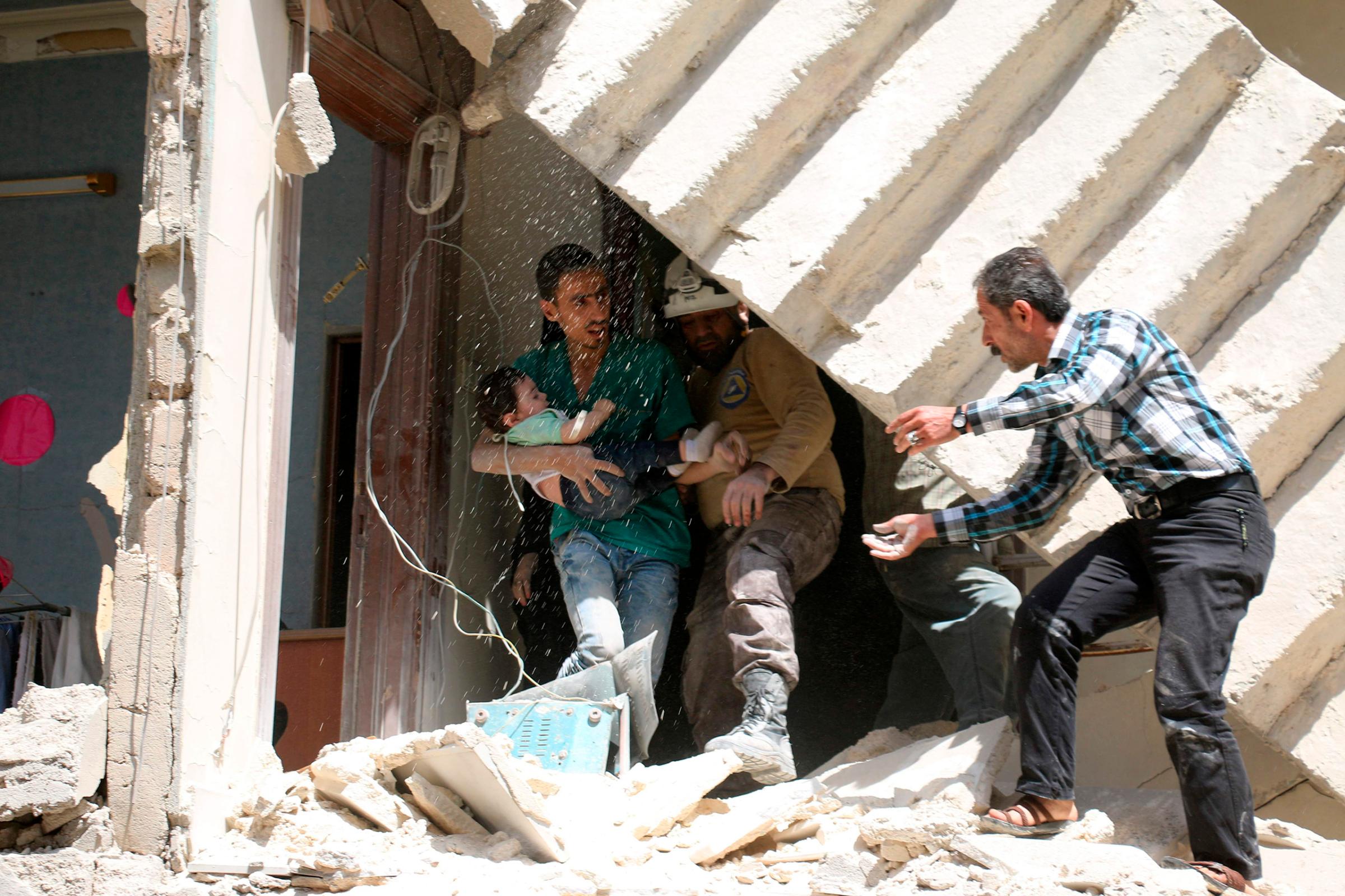 A man helps to evacuated a toddler from a destroyed building following a reported airstrike on a rebel-held neighborhood in Aleppo, Syria, April 28, 2016.