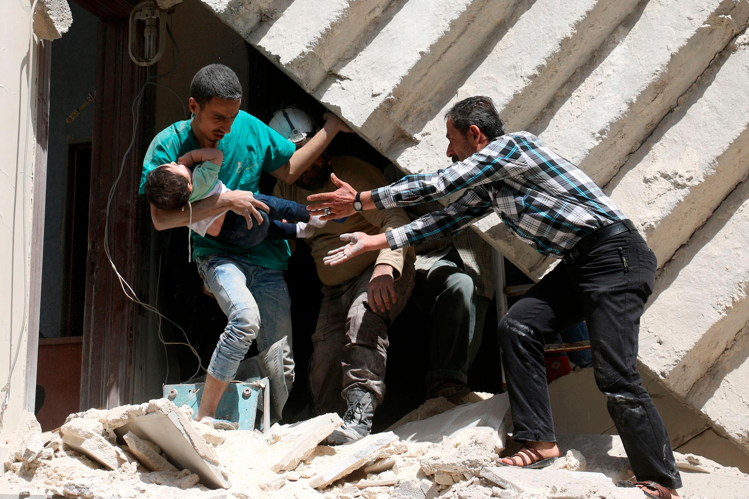 A toddler is passed between men who are evacuating residents from a destroyed building following a reported airstrike on a rebel-held neighborhood in Aleppo, Syria, April 28, 2016.