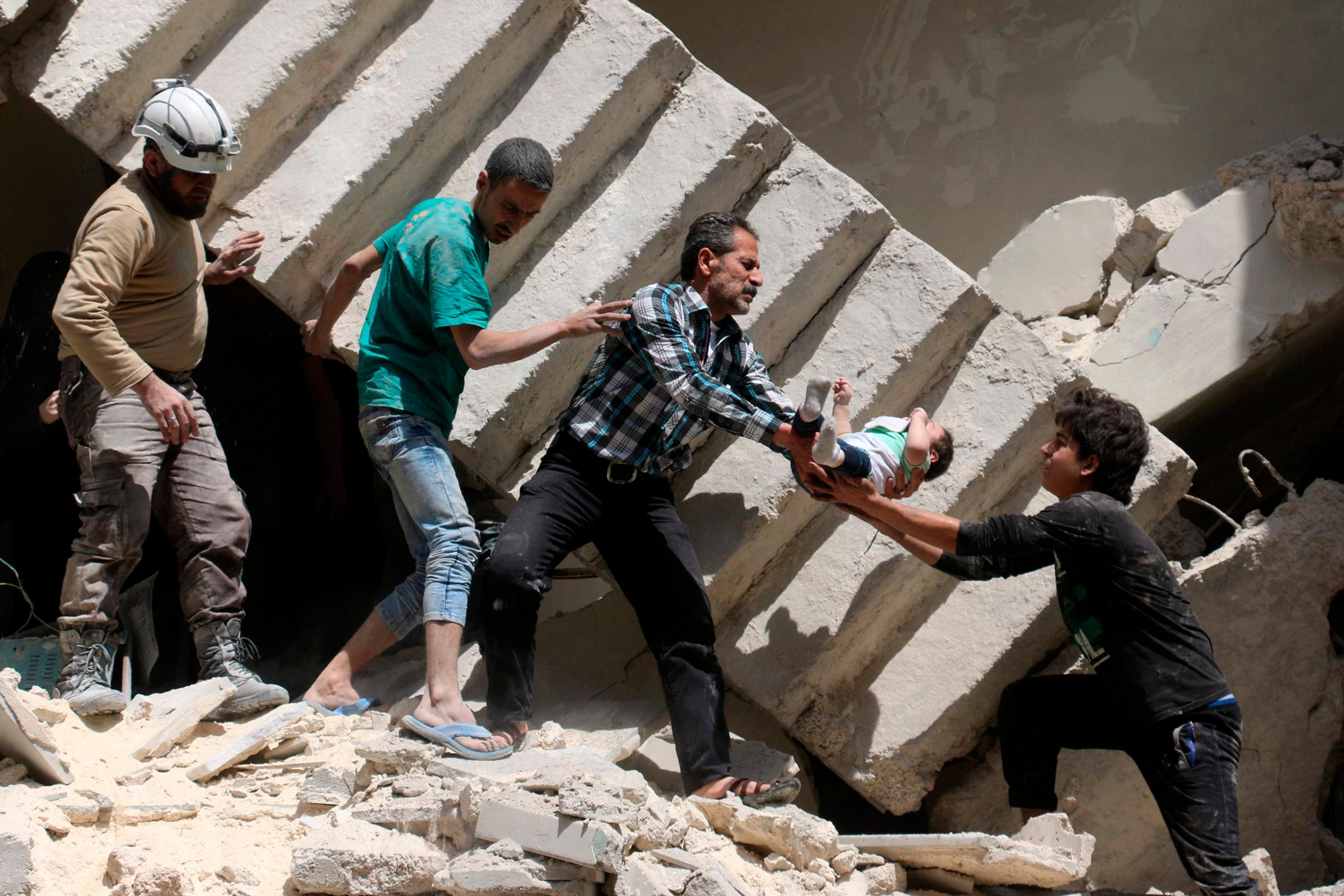 Men pass a toddler between each other during an evacuation from a destroyed building following a reported airstrike on a rebel-held neighborhood in Aleppo, Syria, April 28, 2016.
