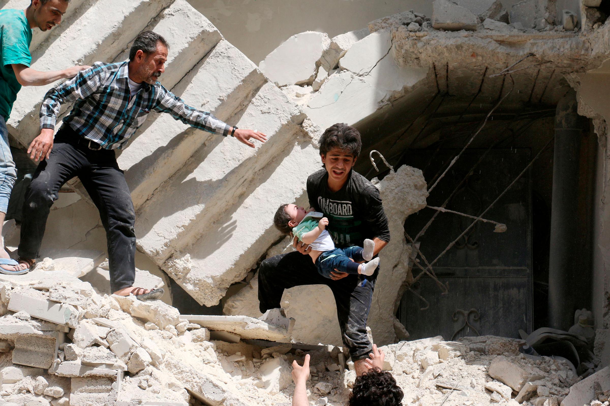 A toddler is evacuated from a destroyed building following a reported airstrike on a rebel-held neighborhood in Aleppo, Syria, April 28, 2016.