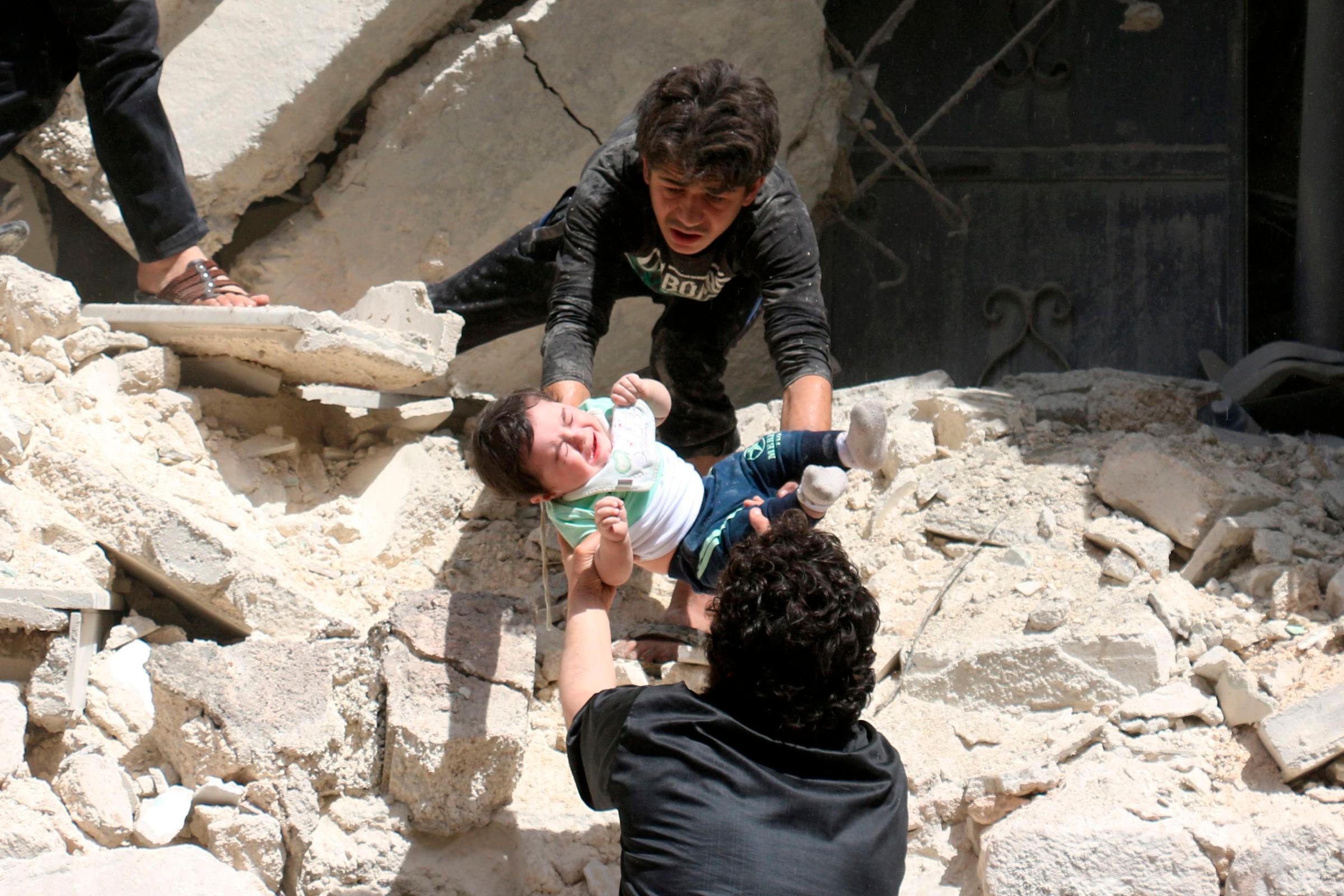 Men evacuate a toddler from a destroyed building following a reported airstrike on a rebel-held neighborhood in Aleppo, Syria, April 28, 2016.