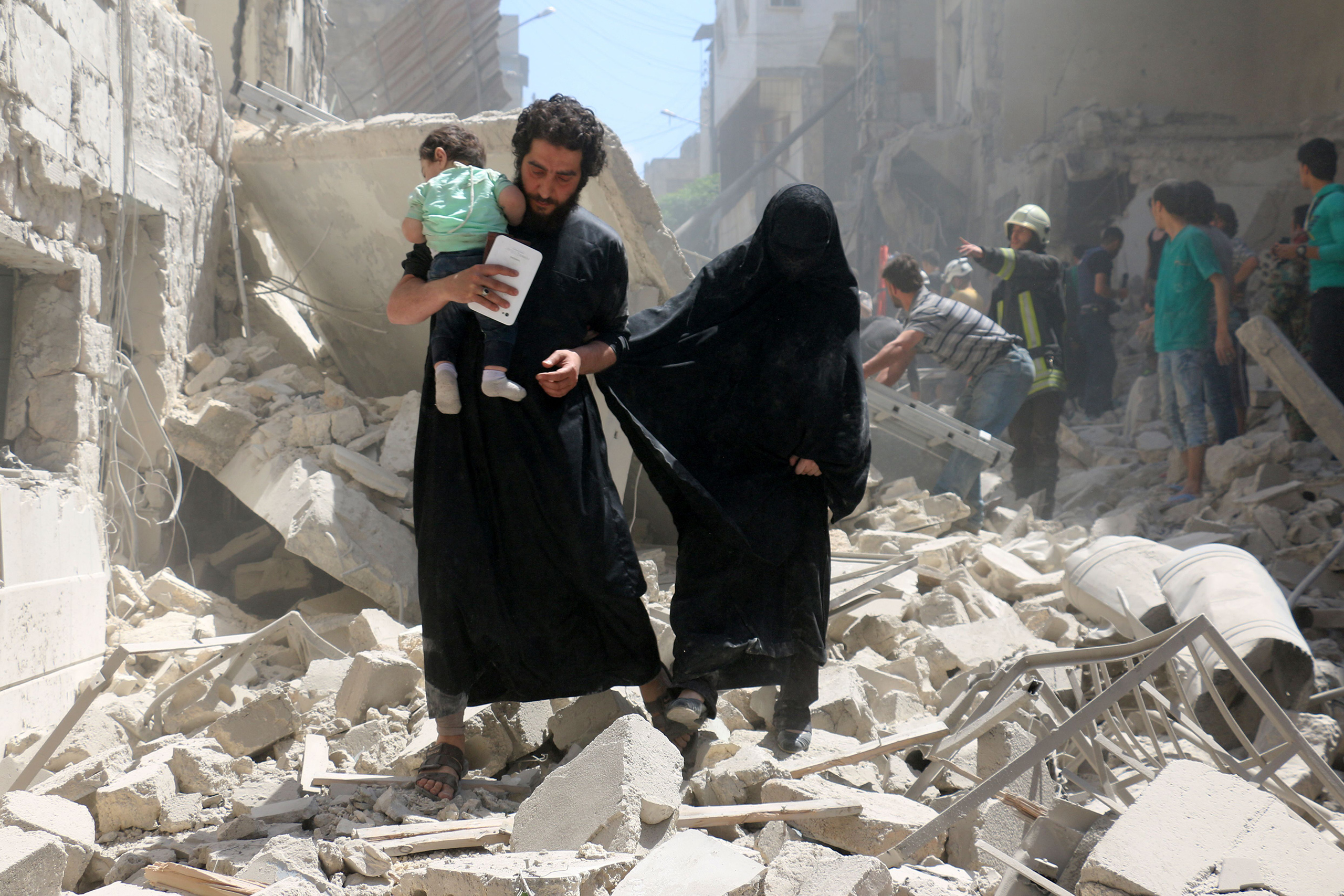 The toddler is held tightly by a man walking with a woman over the rubble. (Ameer Alhalbi—AFP/Getty Images)