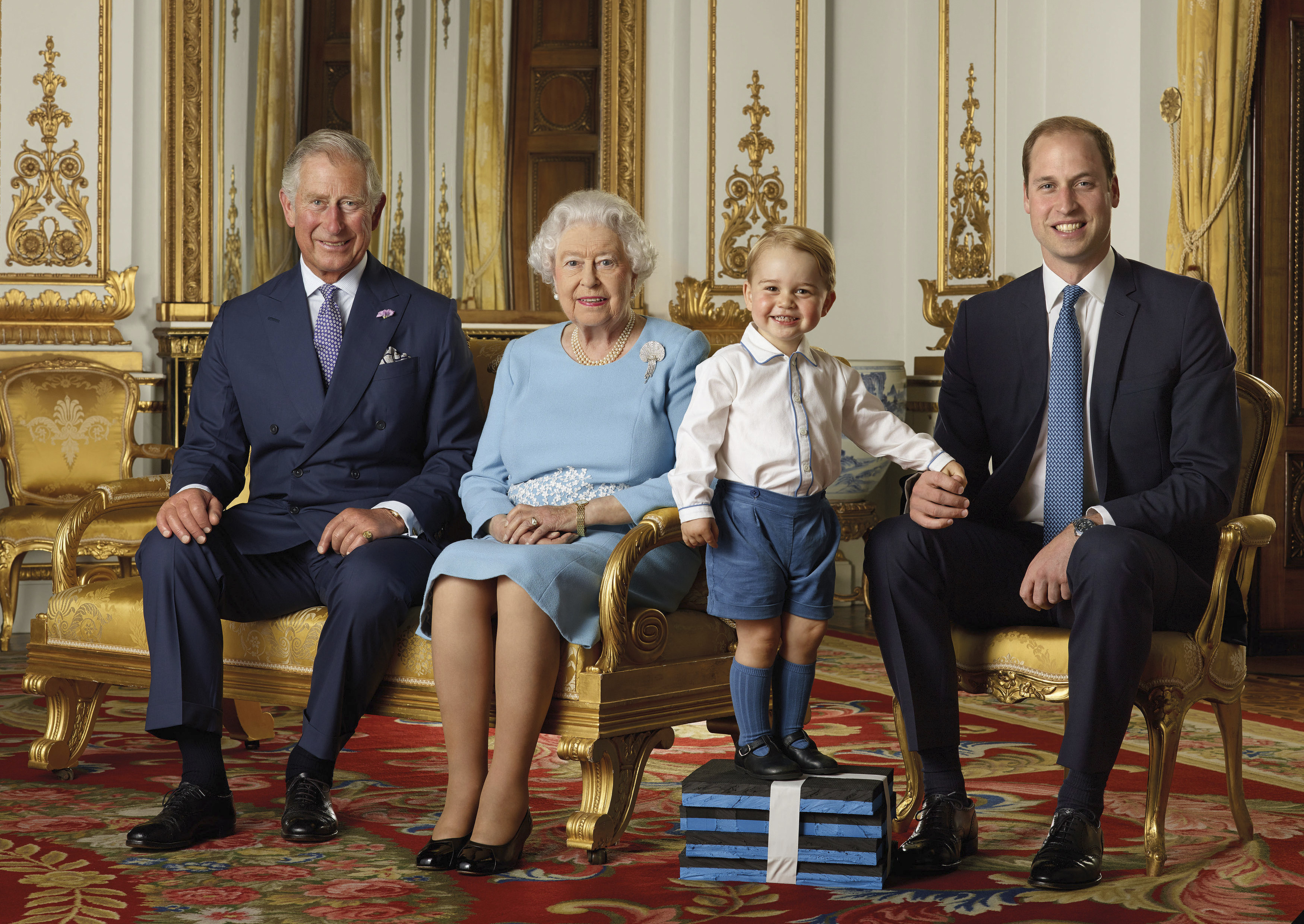 In this image released by the Royal Mail on April 20, 2016, Britain's Prince George stands on foam blocks during a photo shoot in mid-2015 in the White Drawing Room at Buckingham Palace in London, for a stamp sheet to mark the 90th birthday of Britain's Queen Elizabeth II. He is photographed with Prince Charles, Queen Elizabeth II and his father, Prince William, Duke of Cambridge.