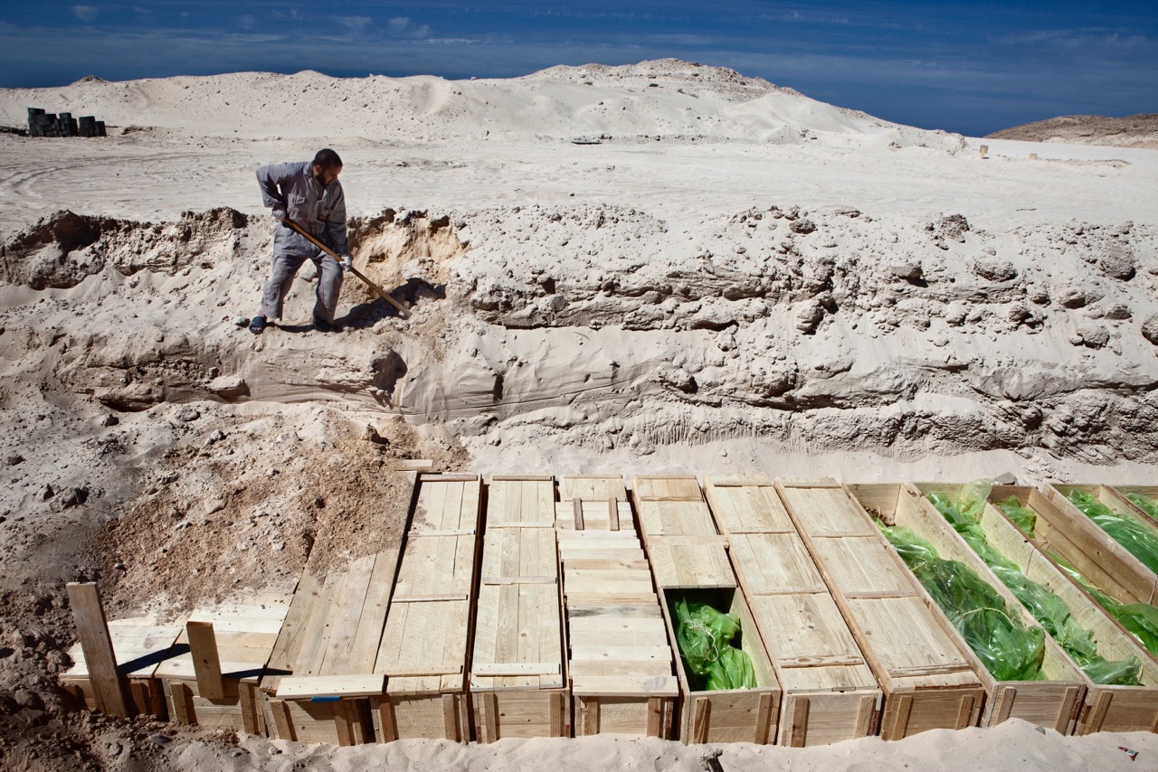A rebel gravedigger buries a row of more than 300 Qadafi government troops killed in combat in the city of Misrata, Libya in 2011.