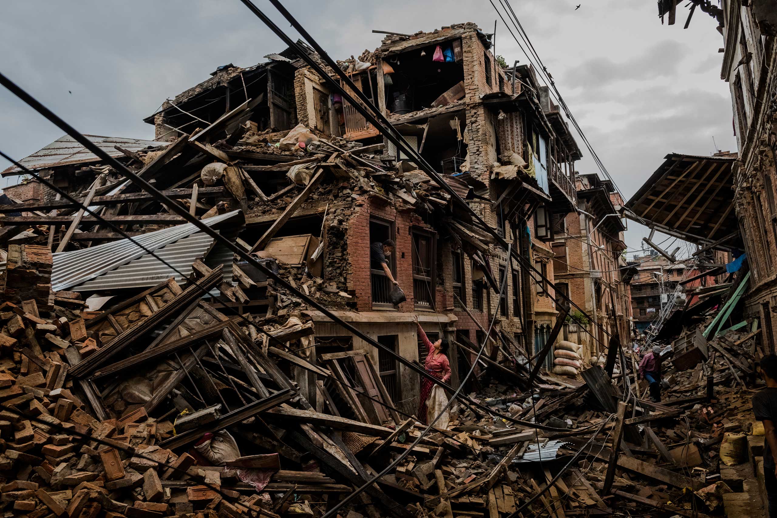 A husband passed salvaged belongings to his wife through the window of their earthquake-destroyed home in Bhaktapur, Nepal. In the days following the 7.8 magnitude quake, residents cautiously returned to collect whatever valuables they could find. April 29, 2015.