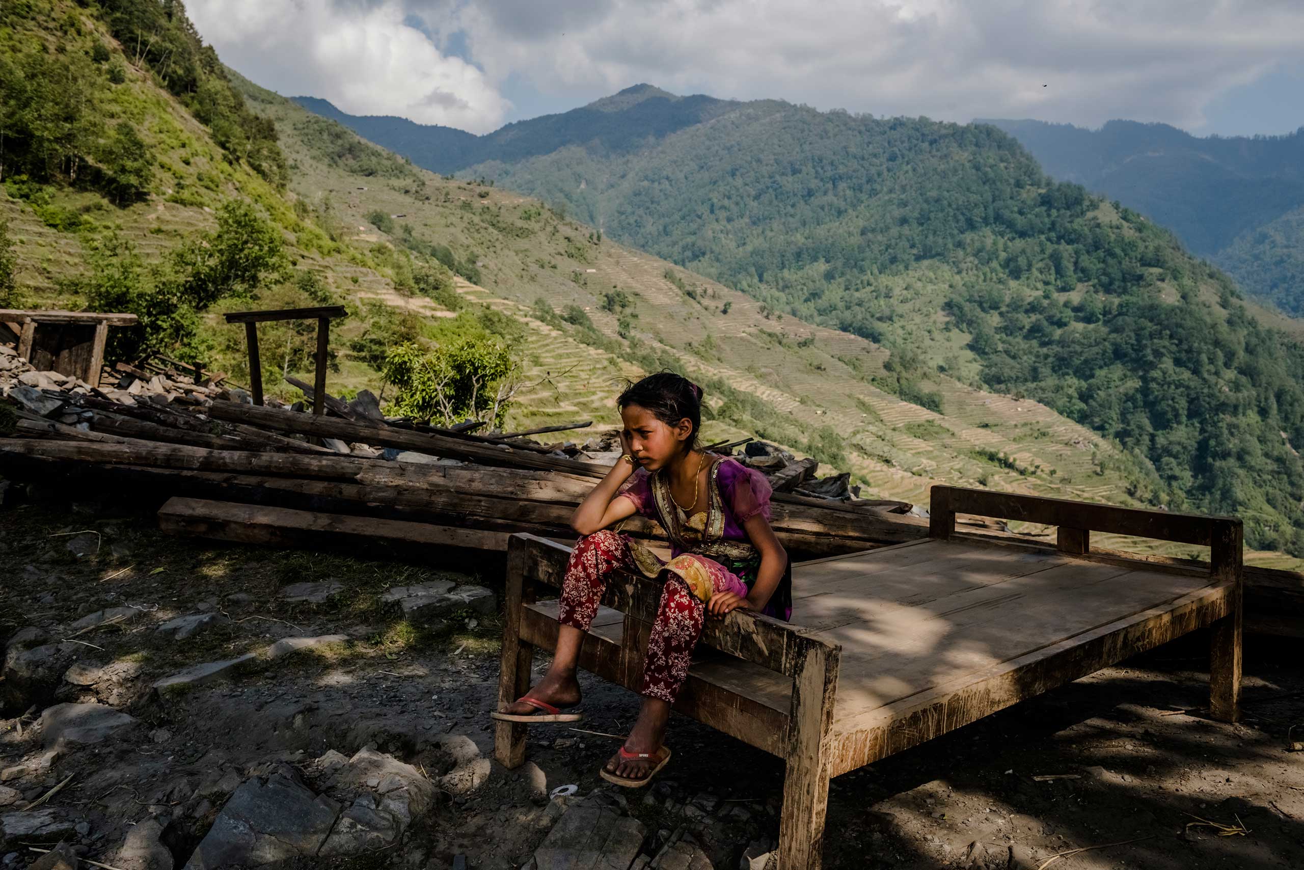A girl rests on a bed frame salvaged from the ruins of her home in the village of Barpak, Nepal. In the village, the epicenter of the April 25 earthquake and one of the larger villages in the mountainous Gorkha district, 1,200 out of 1,475 houses were destroyed. Local authorities said 69 people were killed, 50 were seriously injured and some were still missing. May 5, 2015.