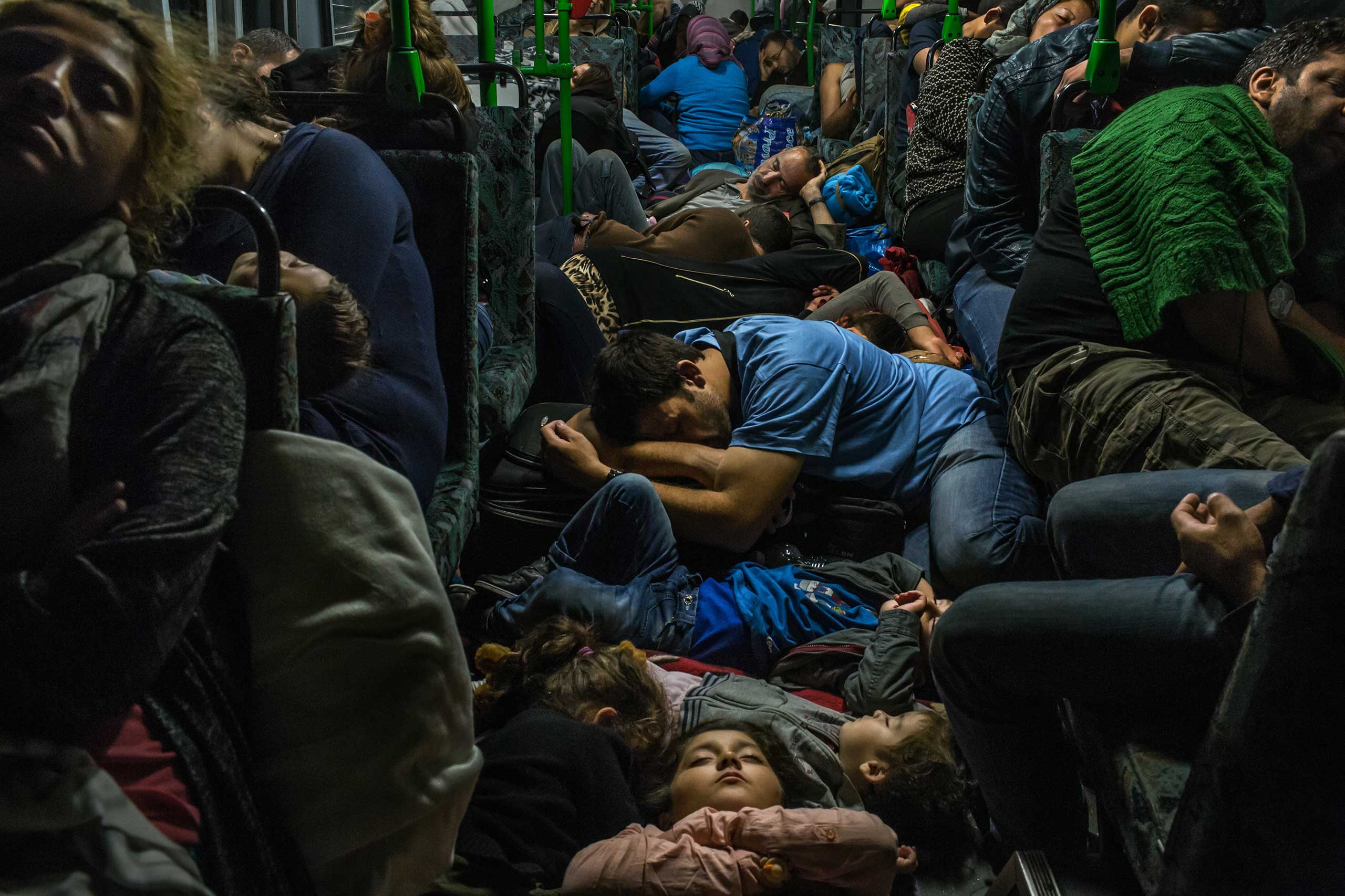 Ahmad Majid, in blue T-shirt at center, sleeps on a bus floor with his children, his brother Farid Majid, in green sweater at right, and other members of their family and dozens of other refugees, after leaving Budapest on the way to Vienna. Sept. 5, 2015.