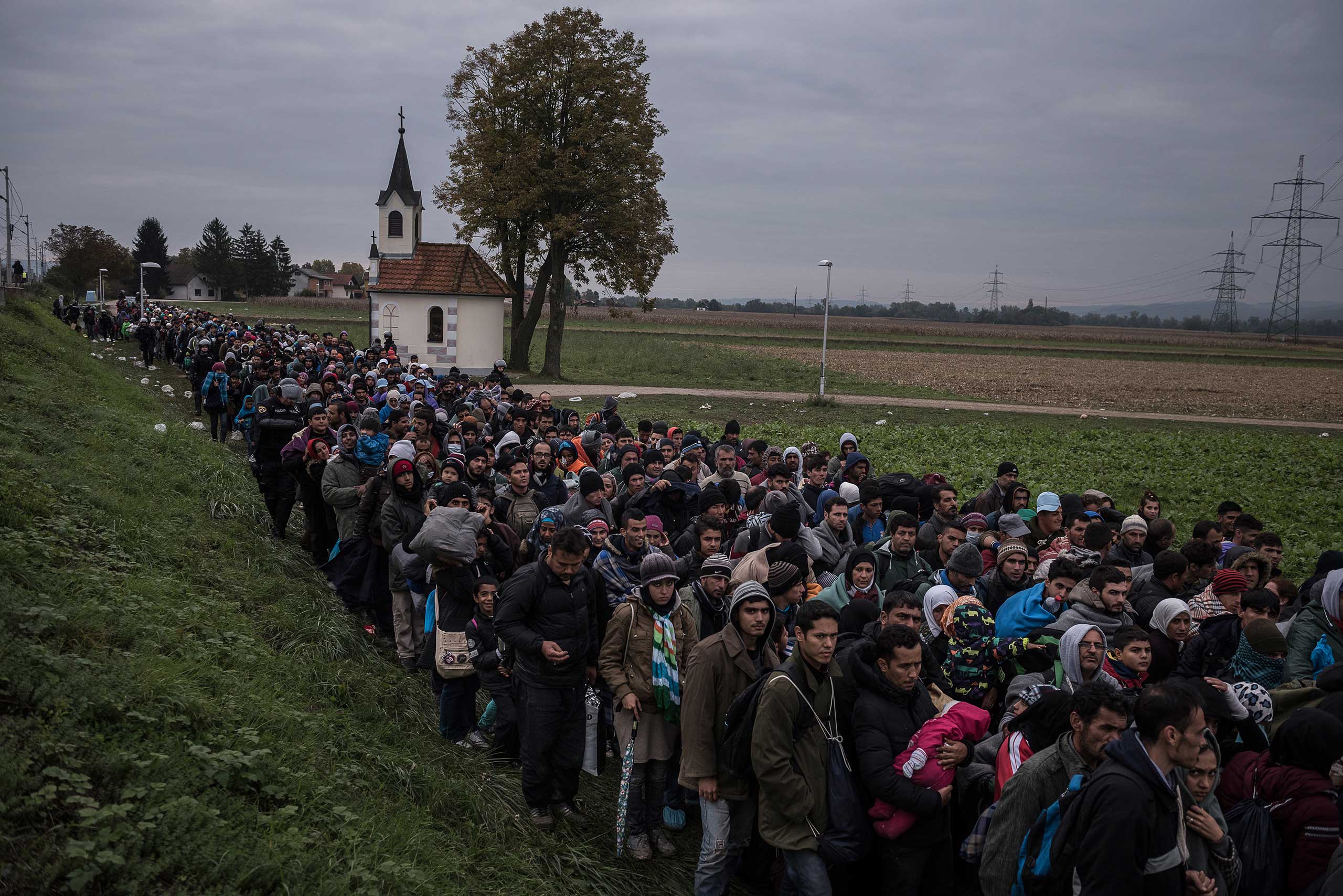Migrants walking past a church, escorted by Slovenian riot police to a registration camp outside Dobova, Slovenia. Oct. 22, 2015.