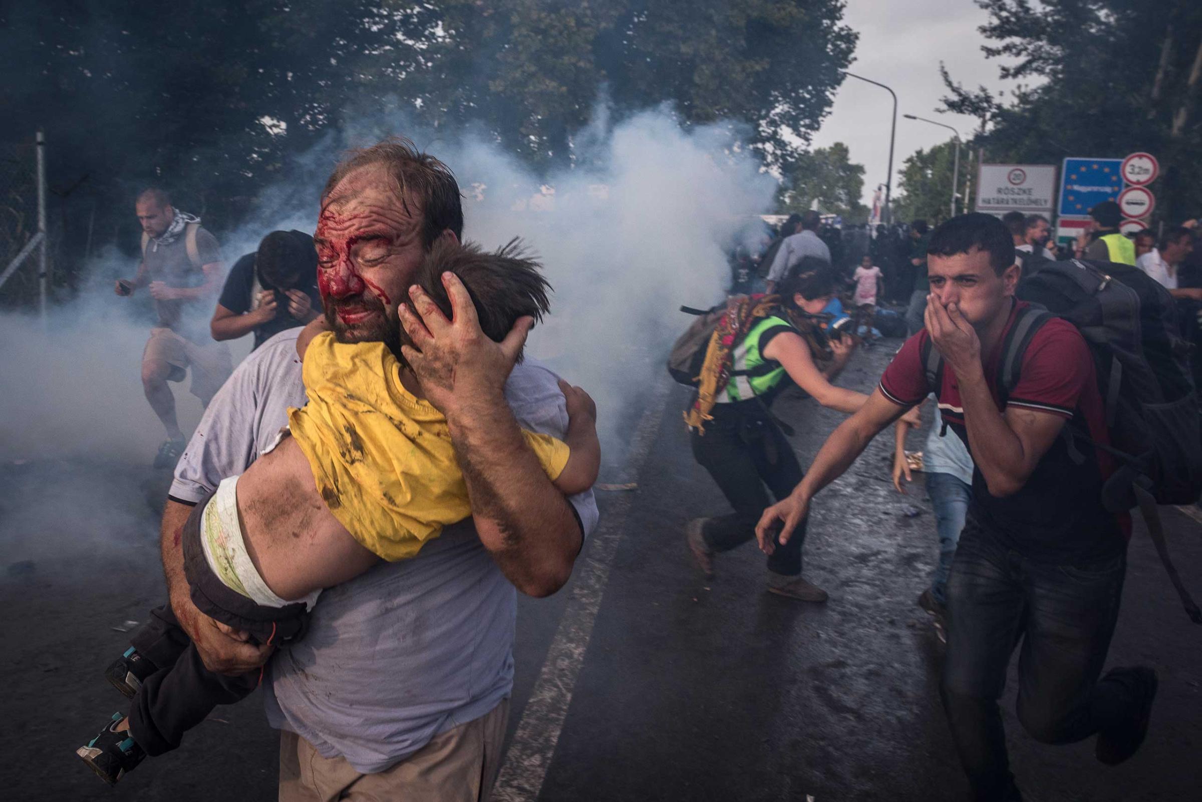 A tries to man shield his child from police beatings and tear gas at the border crossing in Horgos, Serbia. Sept. 16, 2015.
