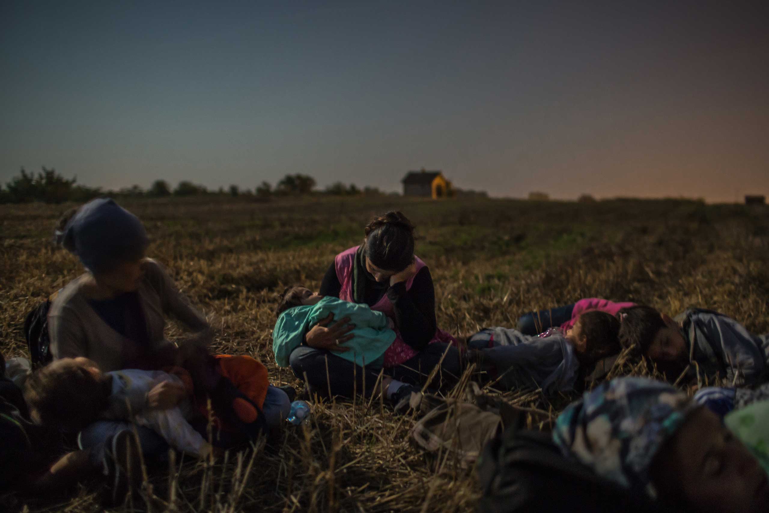 Members of the Majid family from Iraq sleep with their children in their arms in a wheat field as they wait to cross the barbed wire fence at Horgos, Serbia, into Hungary. Aug. 31, 2015.