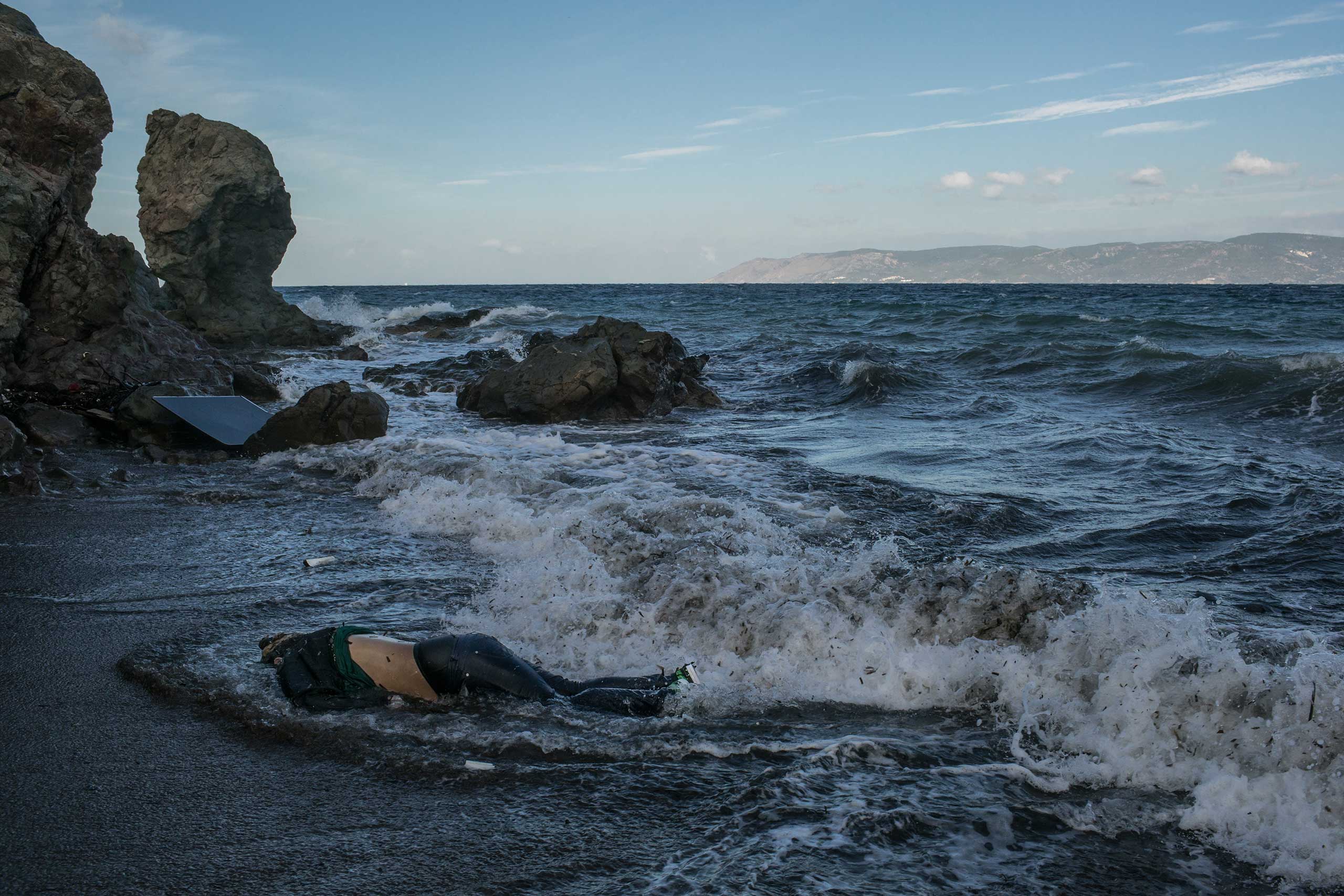 The body of a refugee who attempted to cross the Aegean Sea from Turkey, in the background, on the Greek island of Lesbos. Three other bodies, of a 12-year-old girl, a middle-age man and an elderly man, were also found that morning. Nov. 1, 2015.