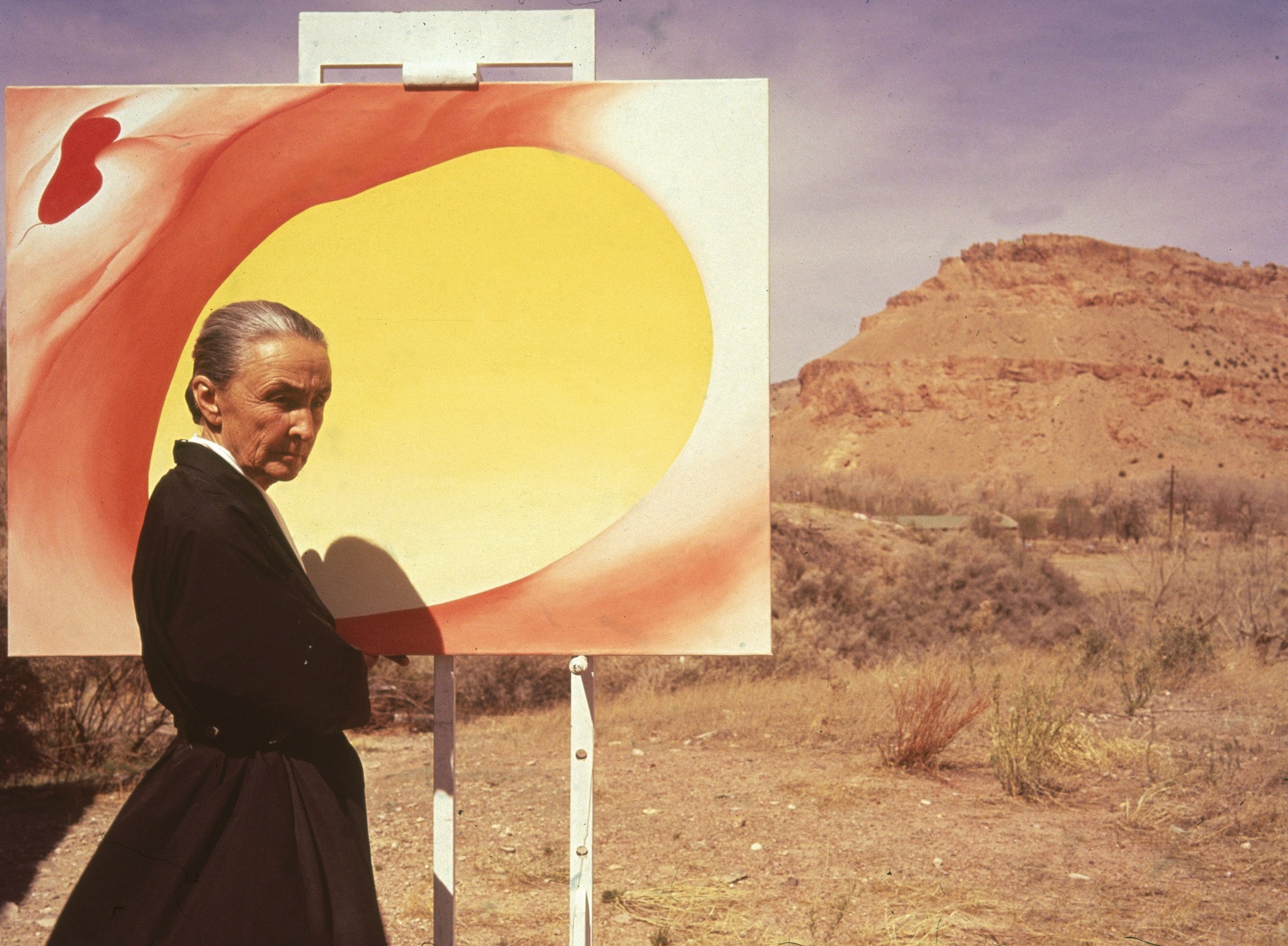 American artist Georgia O'Keeffe (1887 - 1986) poses outdoors beside an easel with a canvas from her series, 'Pelvis Series Red With Yellow,' Albuquerque, New Mexico, 1960.