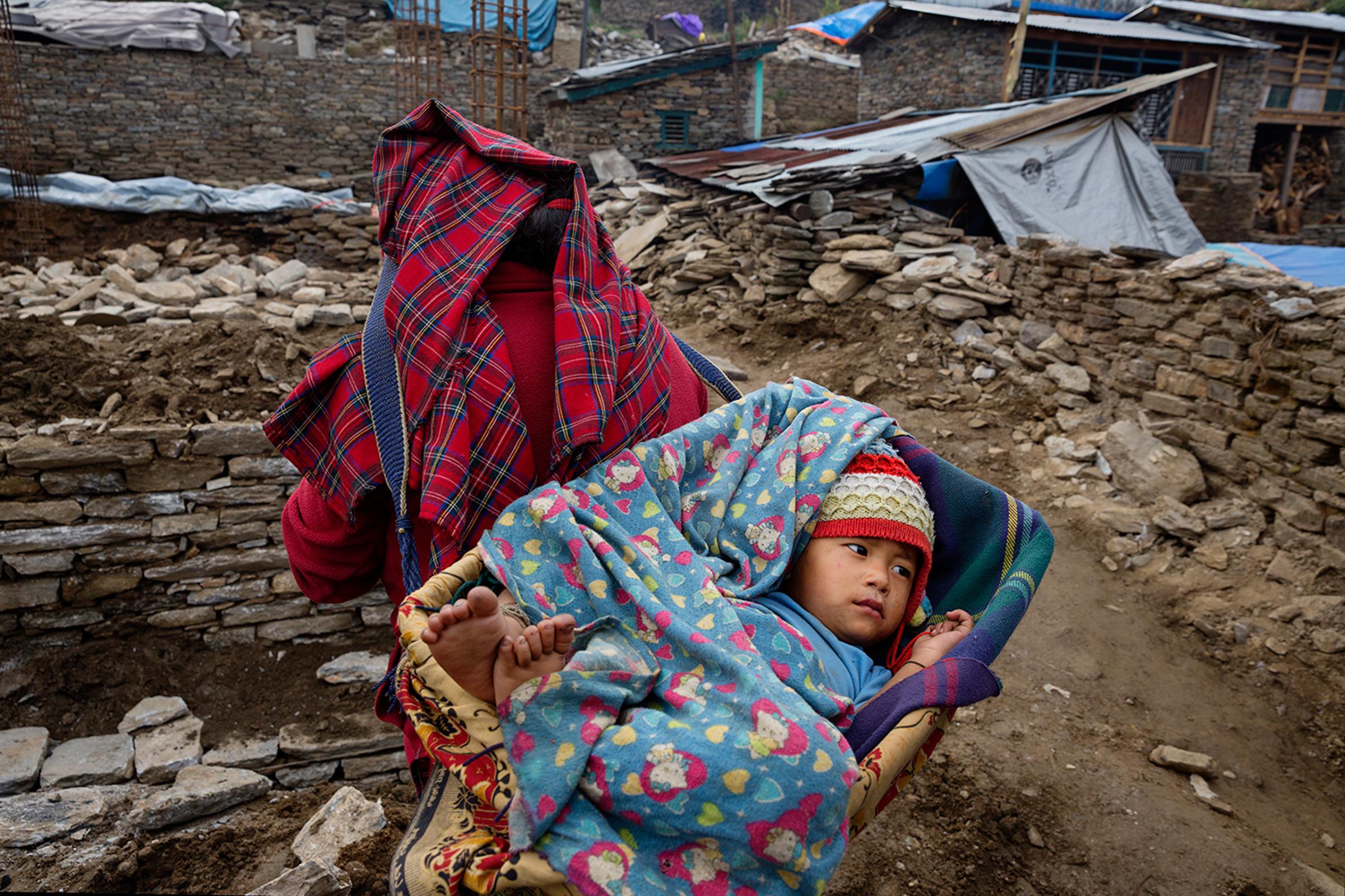 A woman carries a child among wreckage in the village of Barpak, Nepal in Gorkha district, at the epicenter of the 2015 quakes, April 3, 2016.