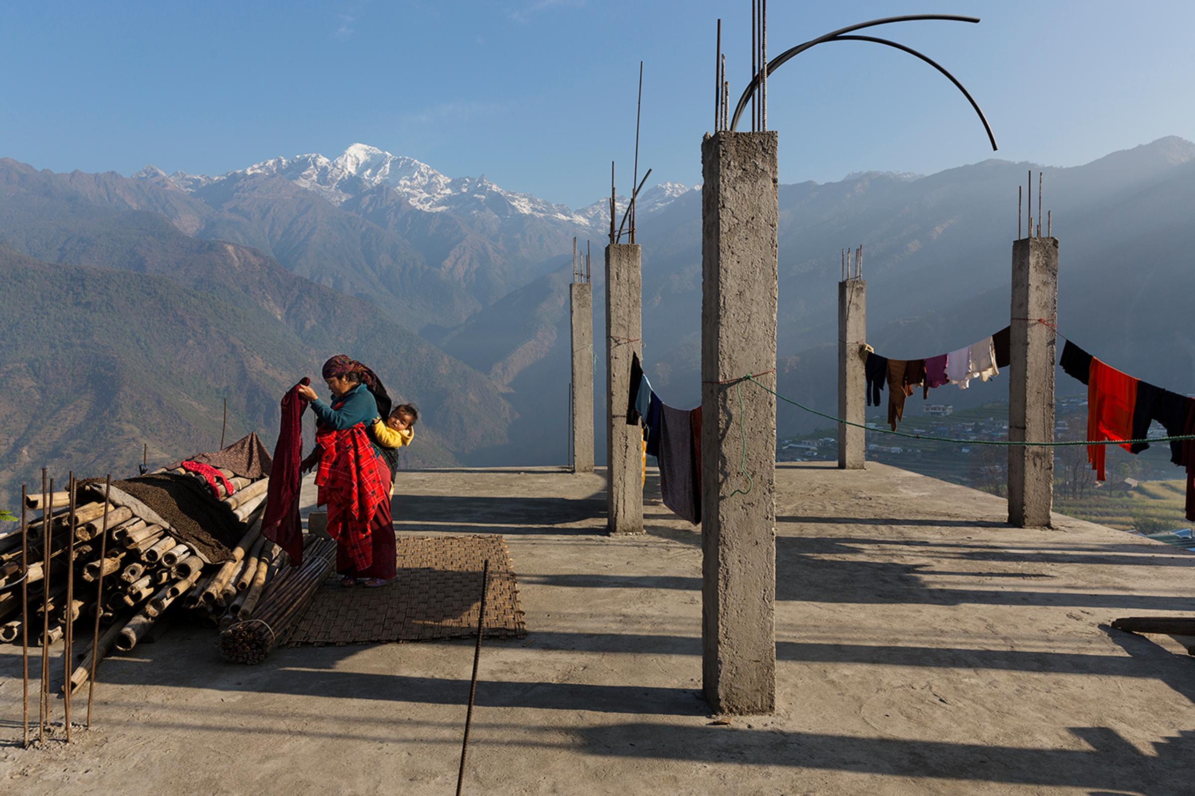 A woman hangs laundry with the Buddha Himal mountain behind her in the Himalyan village of Barpak, in Gorkha district, Nepal. Though international donors stepped up to provide aid in the aftermath of the 2015 quakes, money for rebuilding homes has yet to reach victims. April 6, 2016.