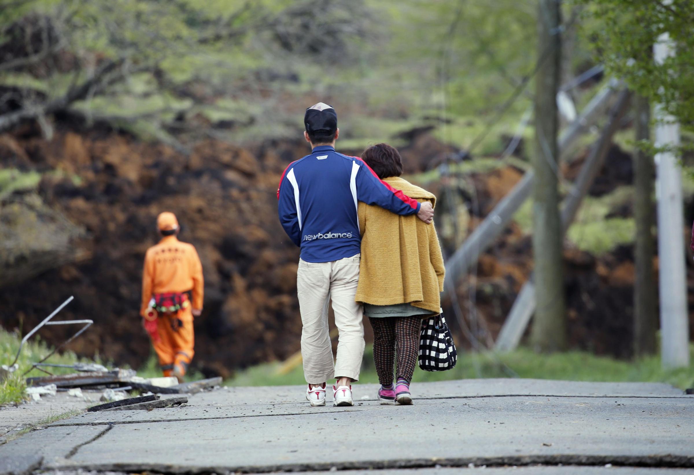 A man hugs his mother as they leave their house buried in a landslide caused by earthquakes in Minamiaso, Kumamoto prefecture, Japan, Sunday, April 17, 2016. Two nights of increasingly terrifying earthquakes flattened houses and triggered major landslides in southern Japan. (Yuki Sato/Kyodo News via AP) JAPAN OUT, MANDATORY CREDIT