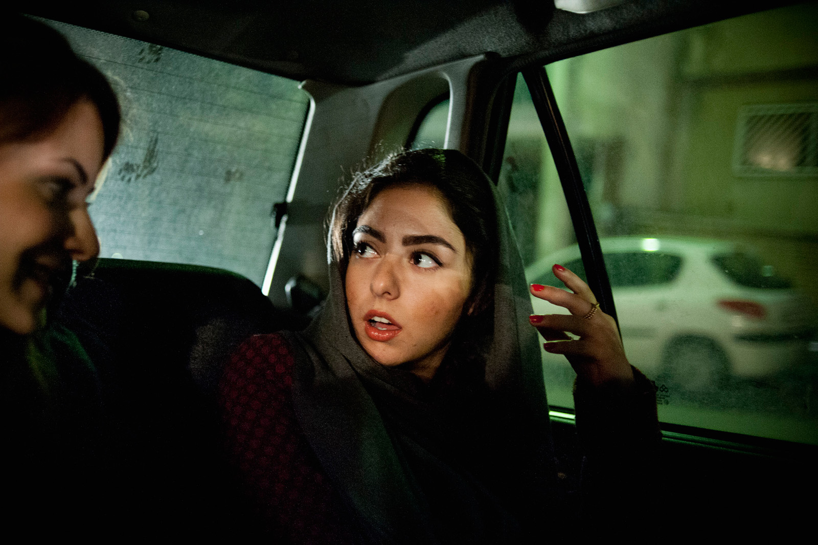 TEHRAN, IRAN | 2011-11-24 | Yassi and her friend take a cab to an opening reception at a gallery in northern Tehran. Even though being bold and eye-catching is always a factor that concerns the morality police, many girls choose to put on bright lipstick and wear distinctive fashion.