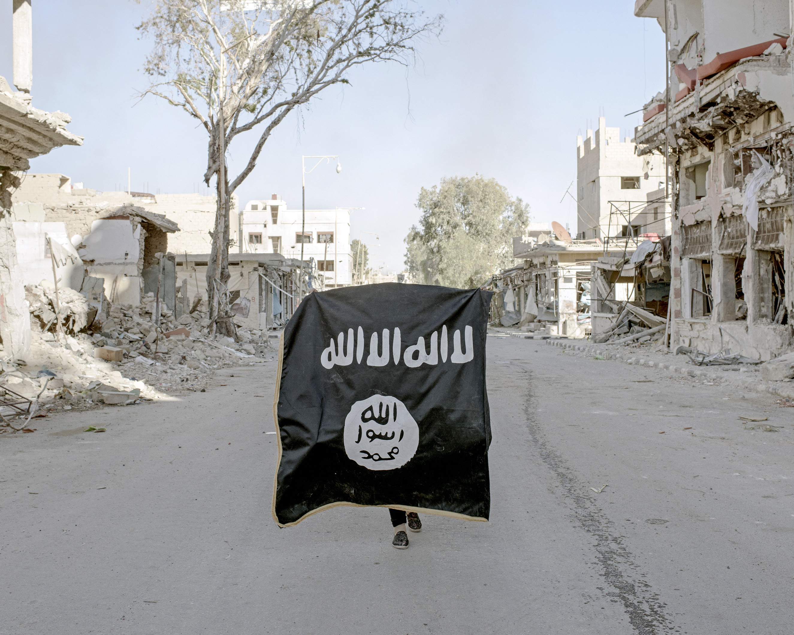 A volunteer soldier from the Syrian National Defense Forces holds up an ISIS flag, discovered in a street of downtown Palmyra, Syria, April 1, 2016.From  Inside War Ravaged Syria