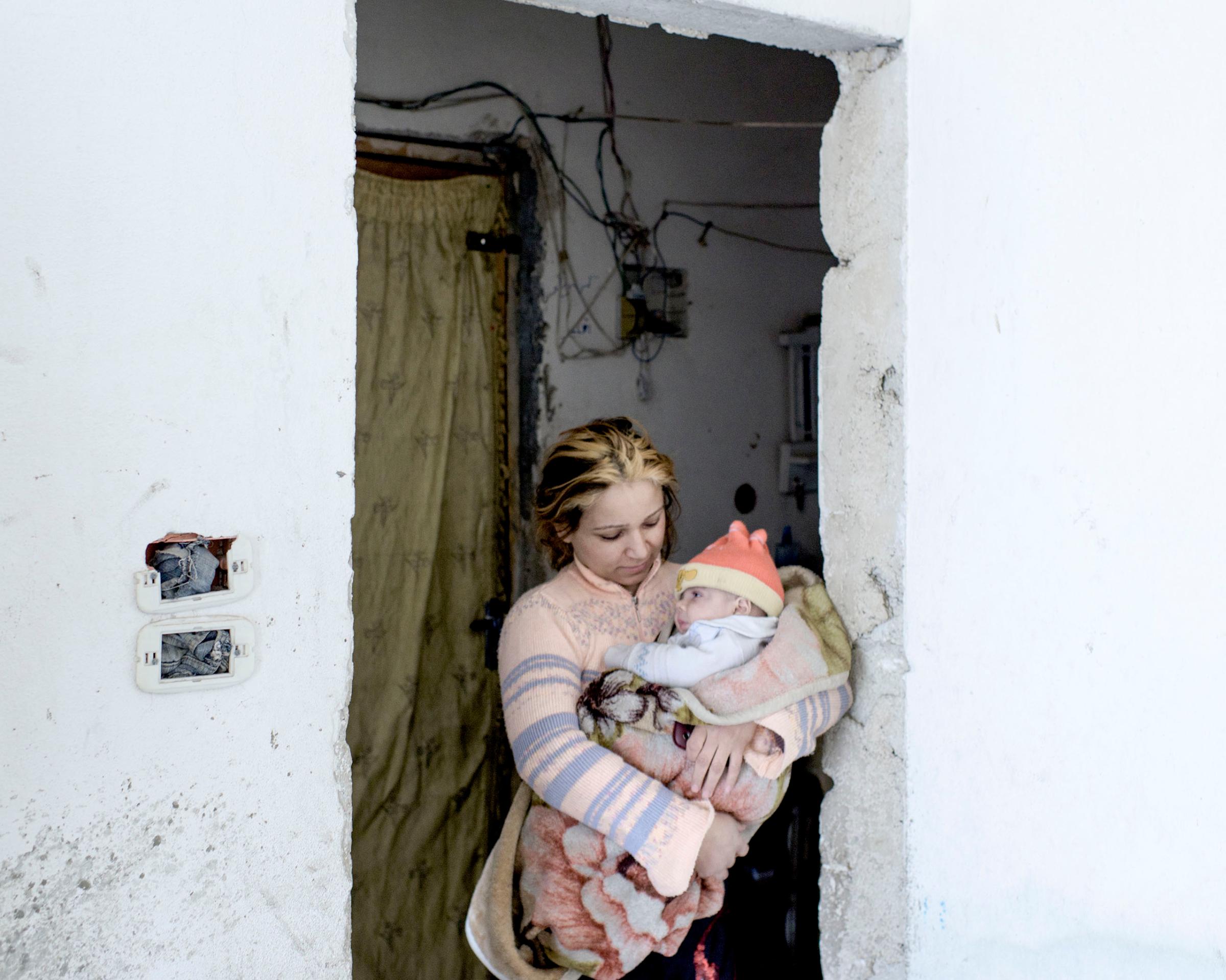 An internally displaced woman holds her baby in the building where they now live in the Salaheddin district of Aleppo, Syria, March 2016.