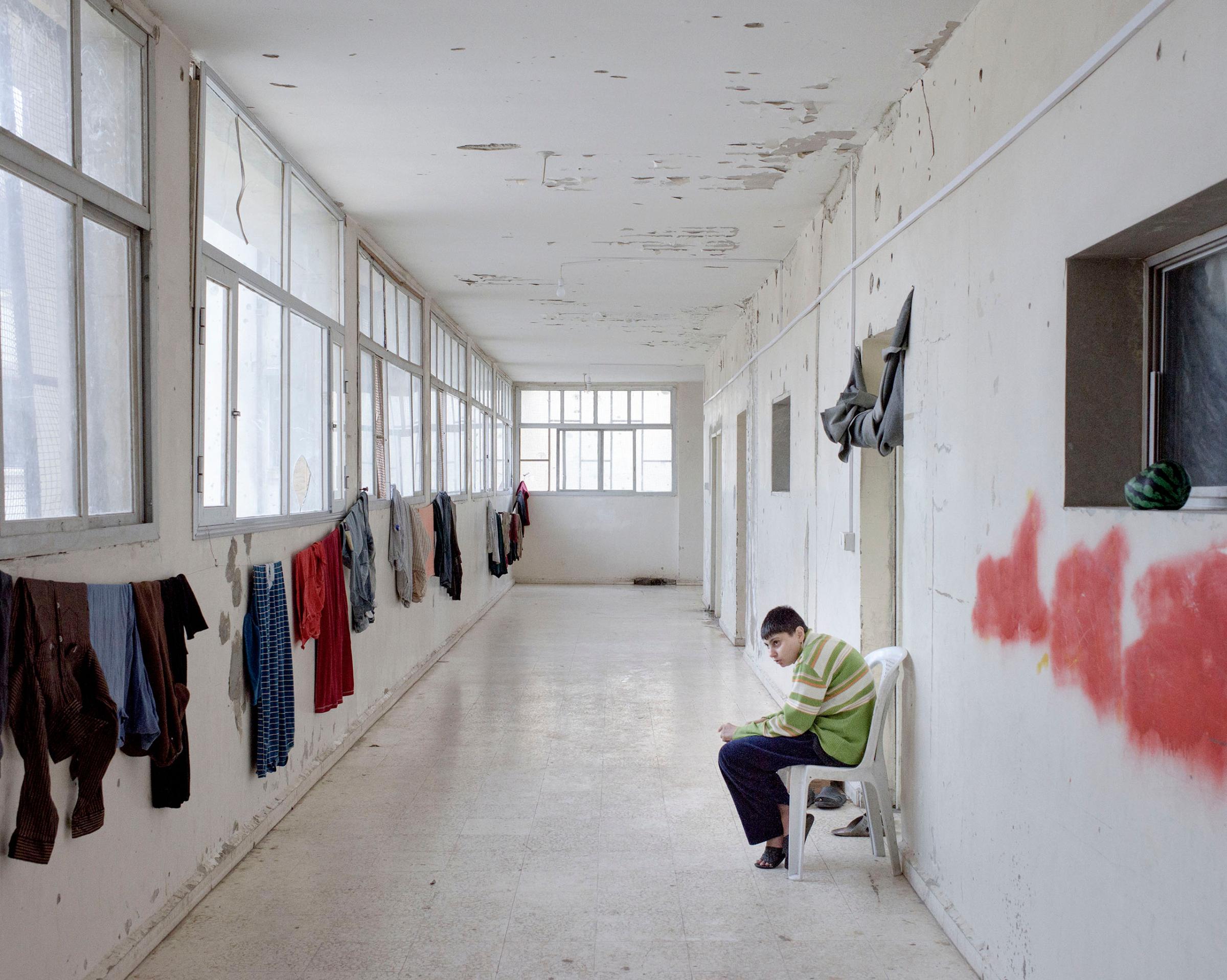 A Syrian boy sits in a hallway of a former school, now a complex used by the Syrian Arab Red Crescent to house internally displaced persons, in the Bab Amr district of Homs, Syria, March 2016.