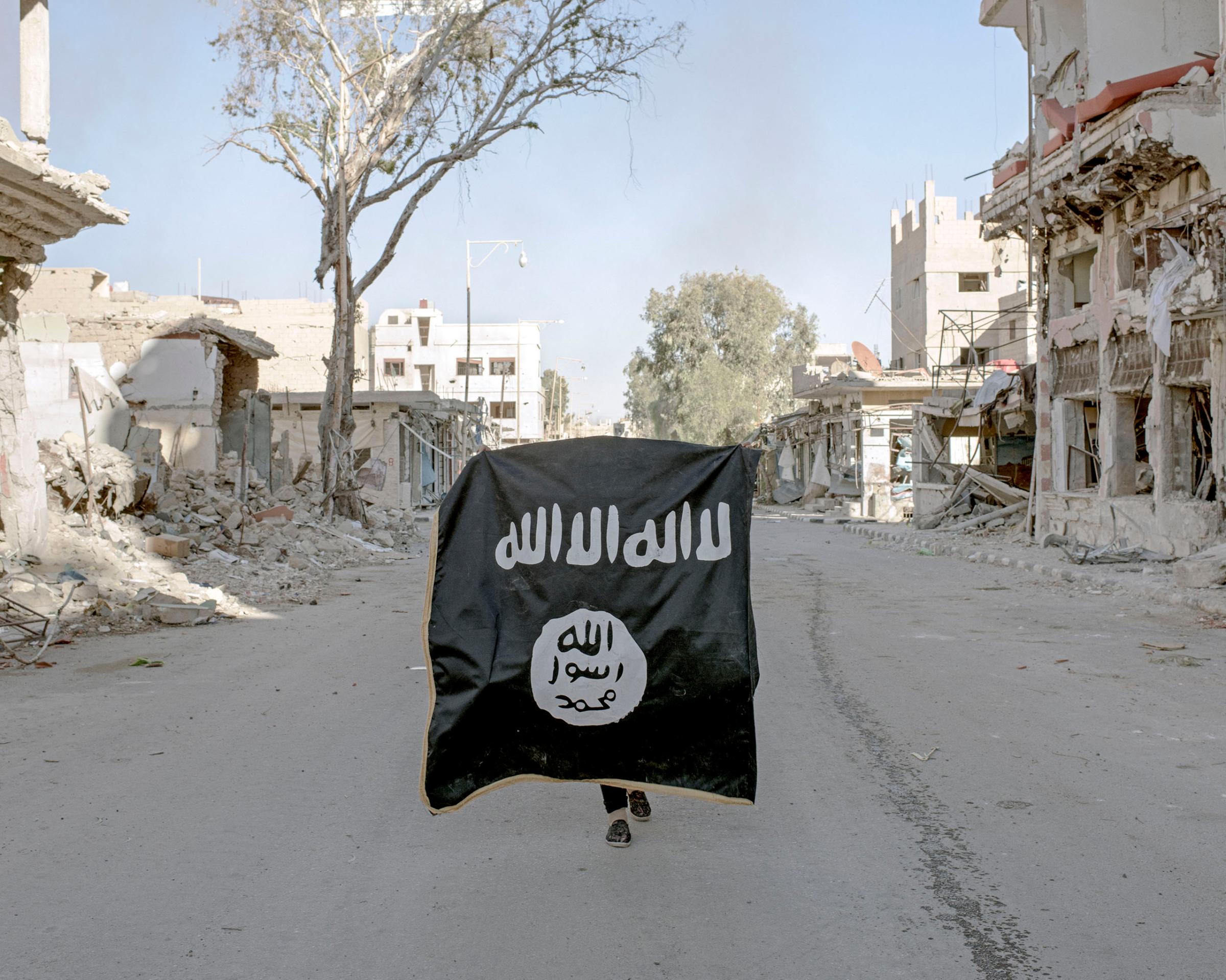 A volunteer soldier from the Syrian National Defense Forces holds up an ISIS flag, discovered in a street of downtown Palmyra, Syria, April 1, 2016.