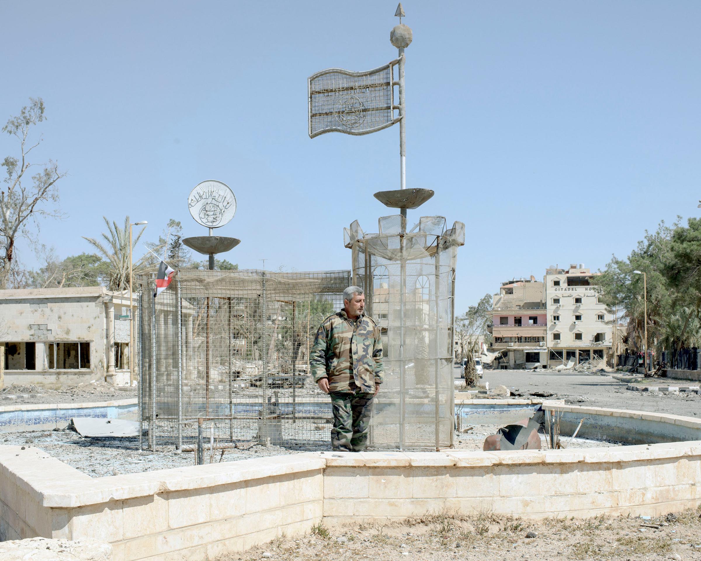 Syrian Army Colonel Samir Ibrahim stands in front of an iron ISIS structure erected in a fountain of the main square in Palmyra, Syria, April 1, 2016. This is where ISIS decapitated Khaled al-Asaad, the octogenarian who headed Palmyra’s antiquities department for decades, stringing up his body to terrify local people.