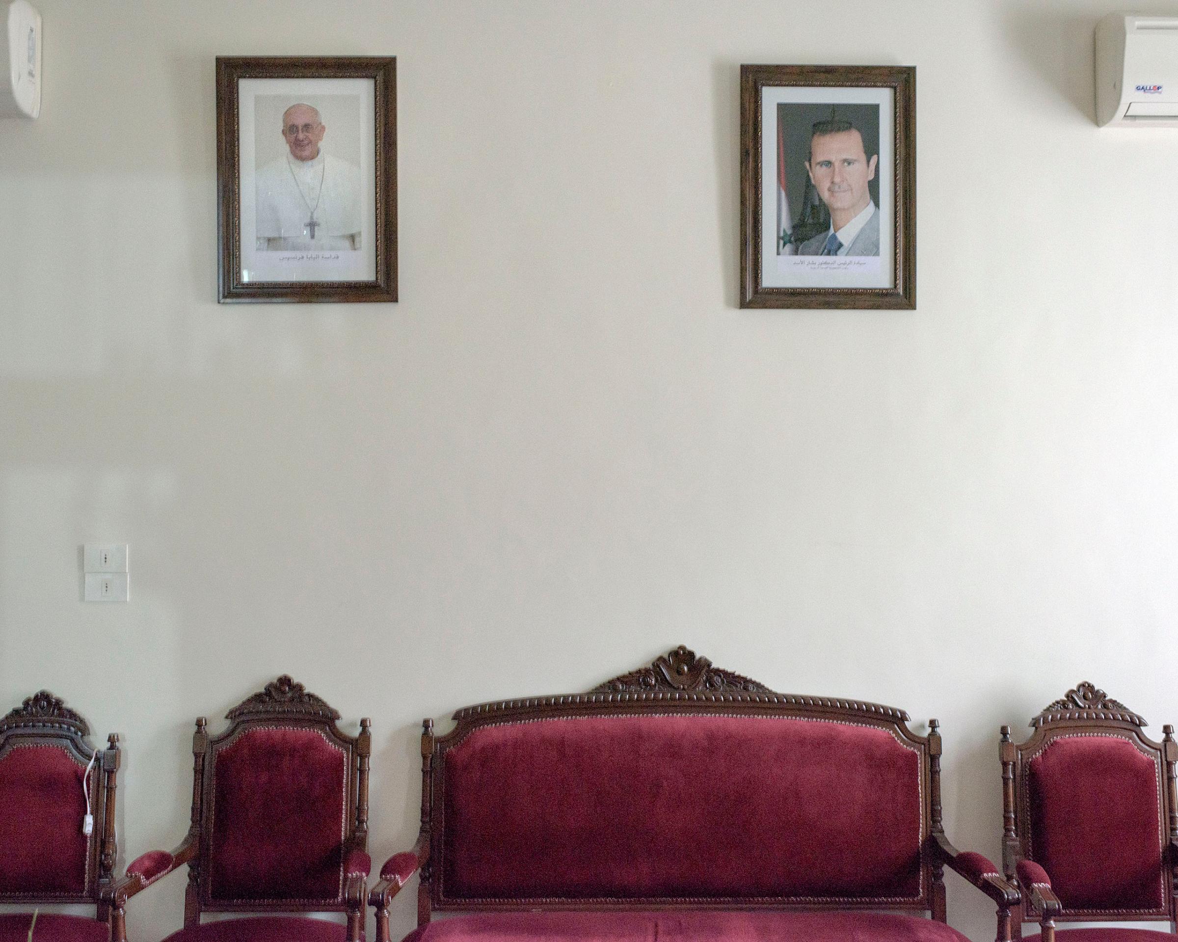 Framed portraits of Pope Francis and Syrian President Bashar Assad hang on a wall inside the offices of the Maronite Bishop of Aleppo, March 2016.