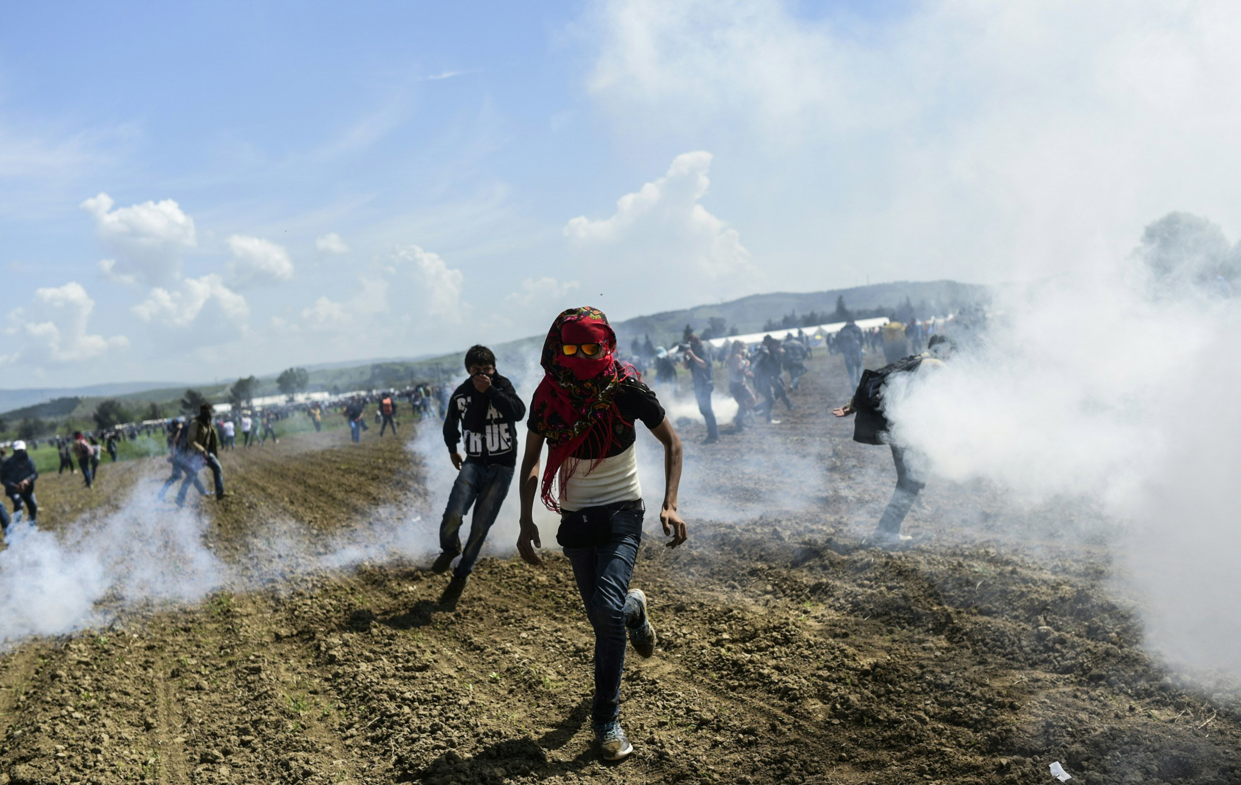 TOPSHOT - Refugees and migrants flee the tear gas as they clash with Macedonian police during a  protest to reopen the border near their makeshift camp in the northern Greek border village of Idomeni, on April 10, 2016. Dozens of people were hurt when police fired tear gas on a group of migrants as they tried to break through a fence on the Greece-Macedonia border, the medical charity Doctors without Borders (MSF) said. A plan to send back migrants from Greece to Turkey sparked demonstrations by local residents in both countries days before the deal brokered by the European Union is set to be implemented. / AFP PHOTO / BULENT KILICBULENT KILIC/AFP/Getty Images