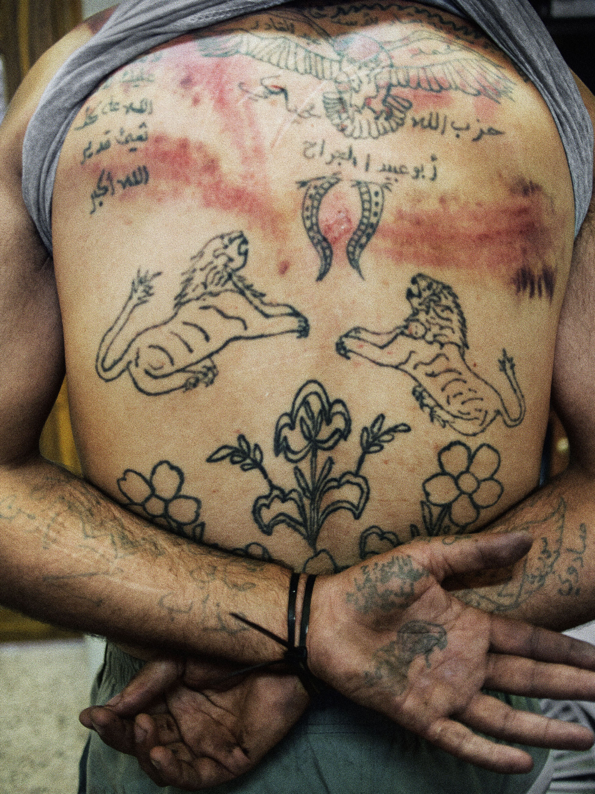 The back of Zakariyya Gazmouz, a suspected Shabiha prisoner, his body covered in pro-Assad tattoos that he later defaced with a razor. Marae, Syria, July 2012.