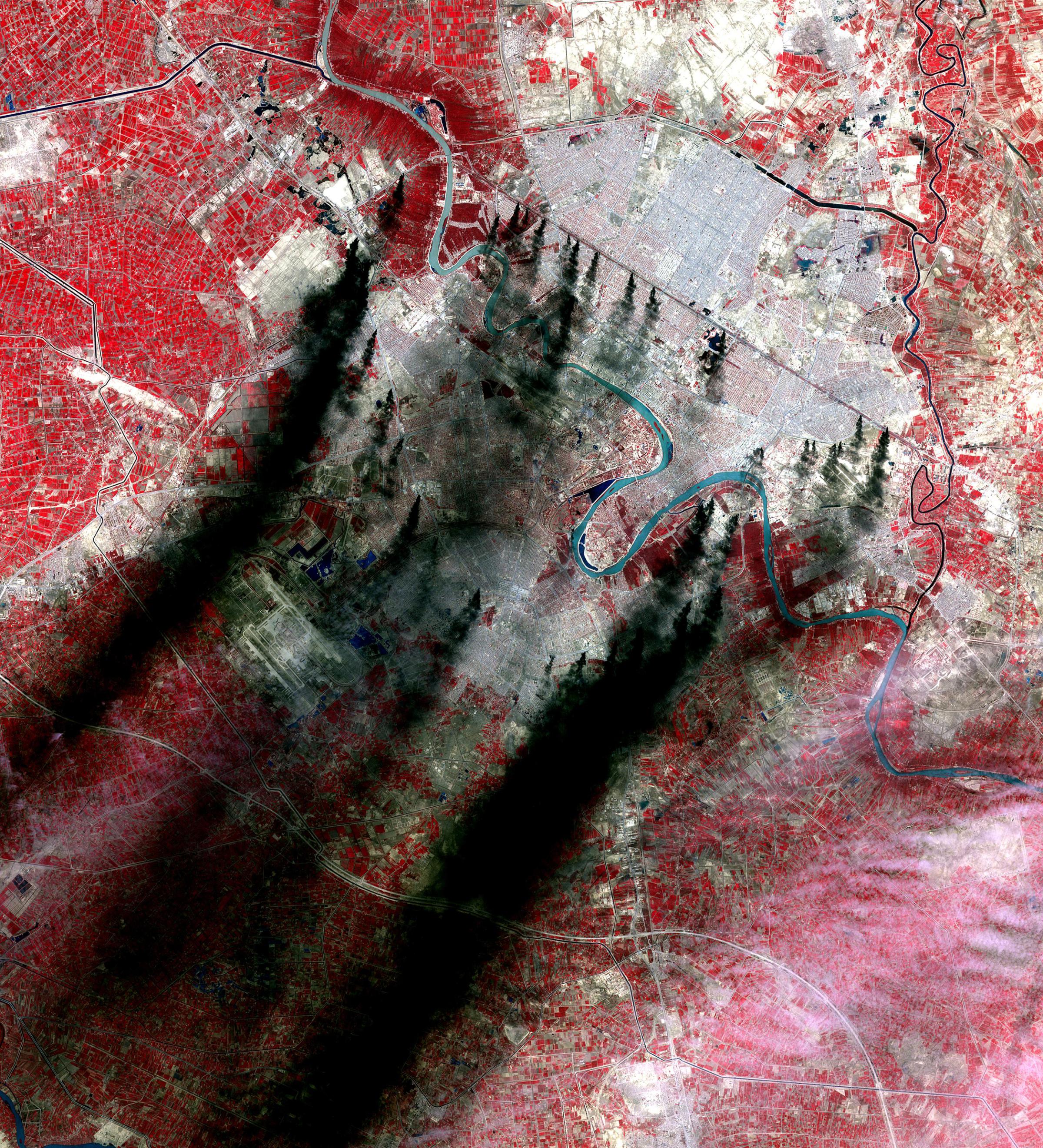 Plumes, believed to be from burning pools of oil from pipelines outside of Baghdad, Iraq, create an environmental health hazard for residents of the city and surrounding regions. The near-infrared wavelengths captured here show vegetation as red. The image was acquired on March 31, 2003.