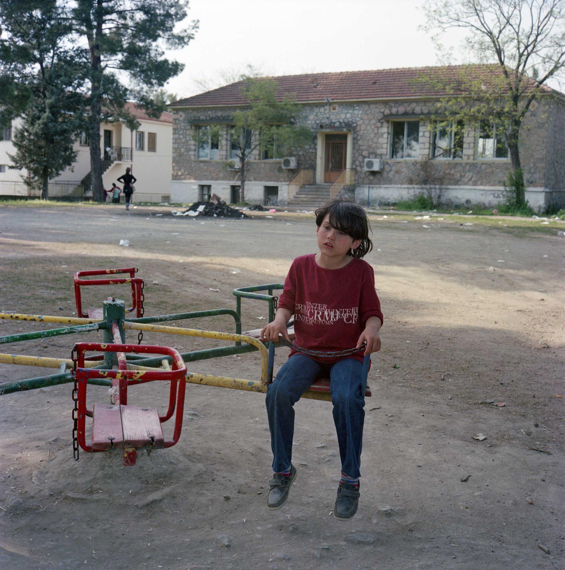 Syrian girl playing in a park outside a school in Idomeni. The school has been used as a storage for food supplies until it was recently looted. Idomeni, Greece. April, 2016