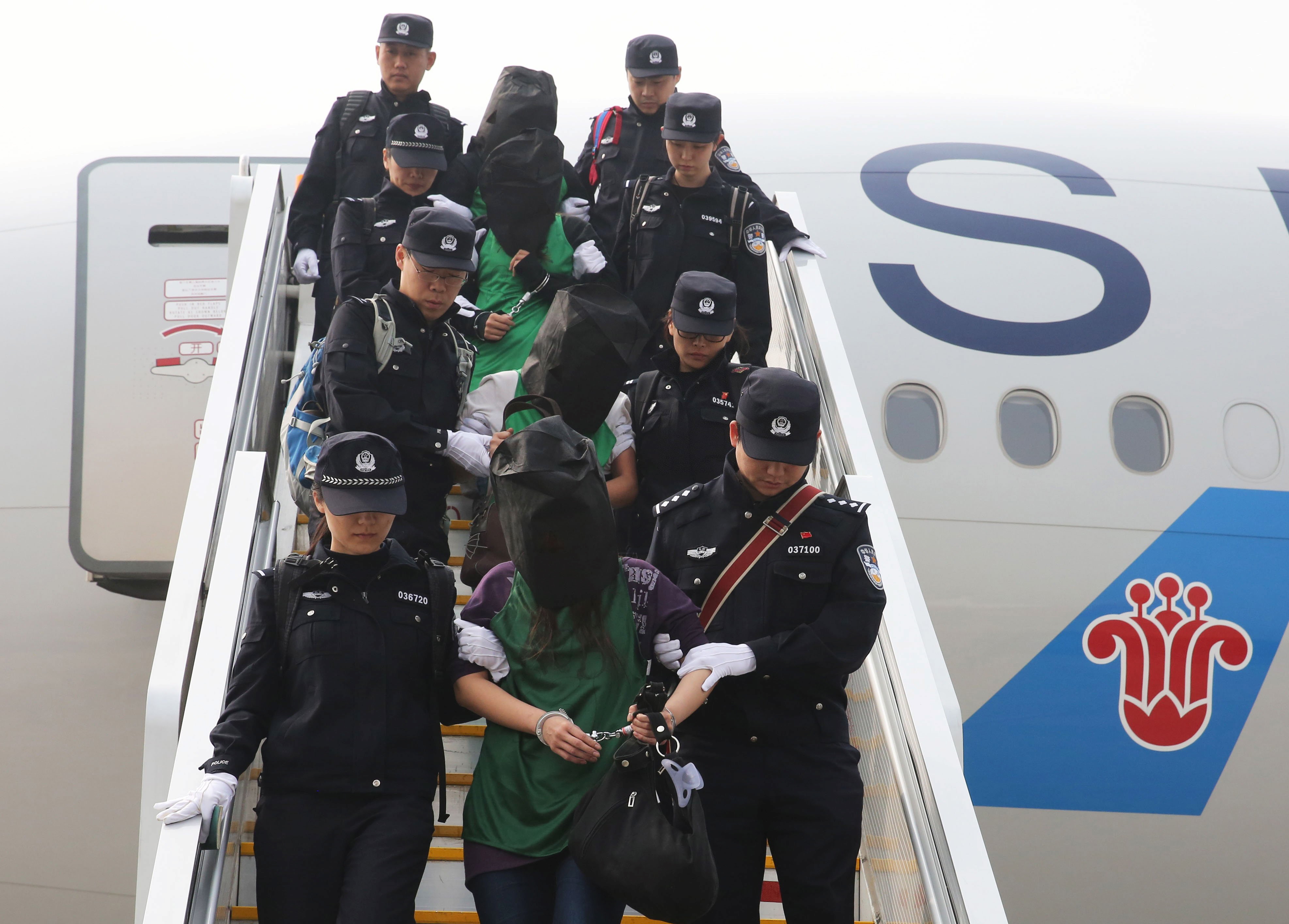 Police escort a group of people wanted for suspected fraud in China, after they were deported from Kenya, as they get off a plane after arriving at Beijing Capital International Airport in Beijing, China