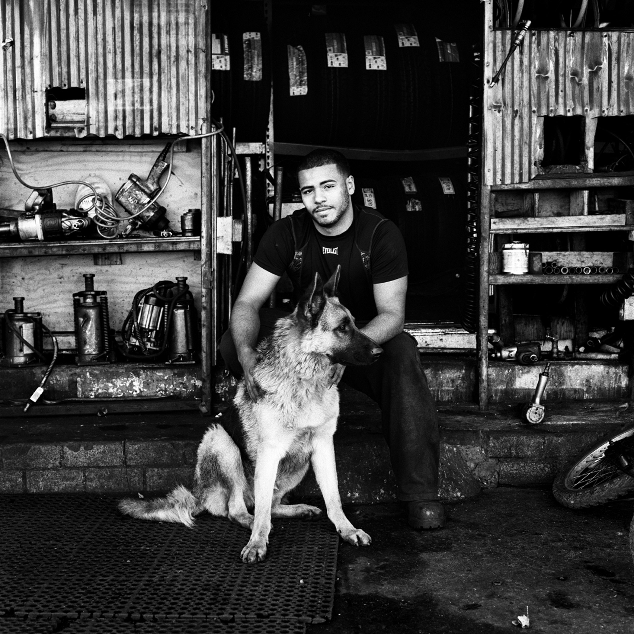 Anthony and his dog Riley at the entrance to their tire shop, P&amp;J Tire Shop, on Metropolitan Avenue in Bushwick, Brooklyn, N.Y., November 2015.