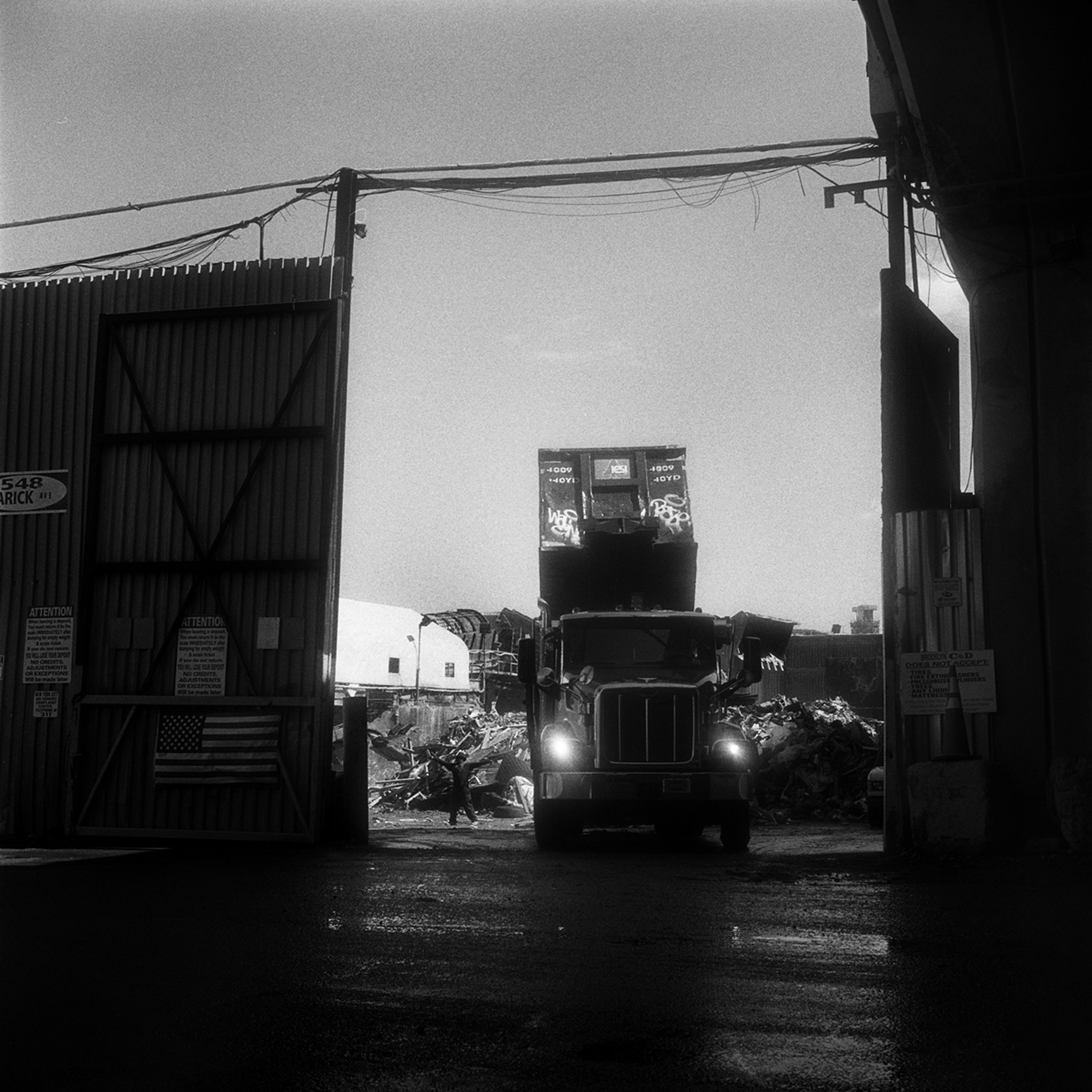 A roll-off truck with its container in the dumping position, as the yard spotter signals to the driver that his container is empty in Greenpoint, Brooklyn, N.Y., September 2015.