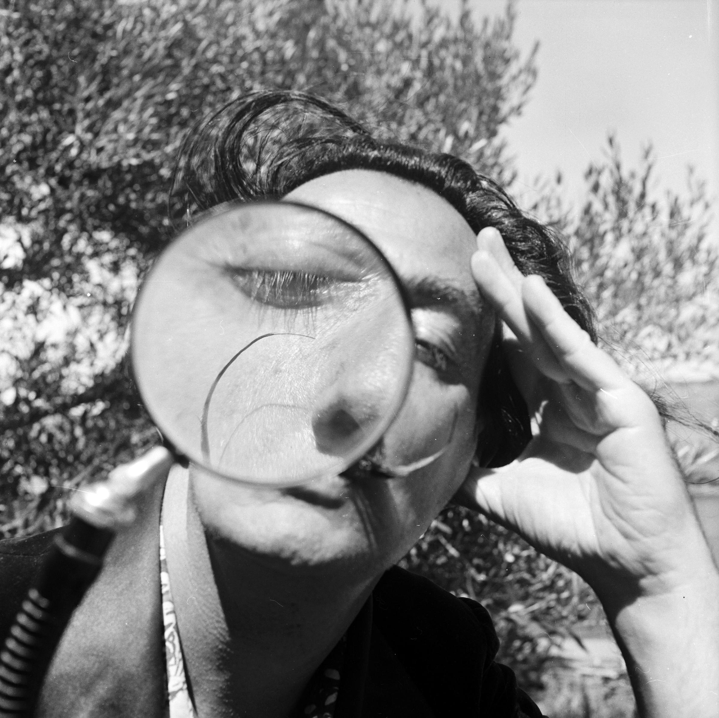 Salvador Dali viewing the camera through a magnifying glass at his home in Cadaques on the Spanish Costa Brava. 1955.