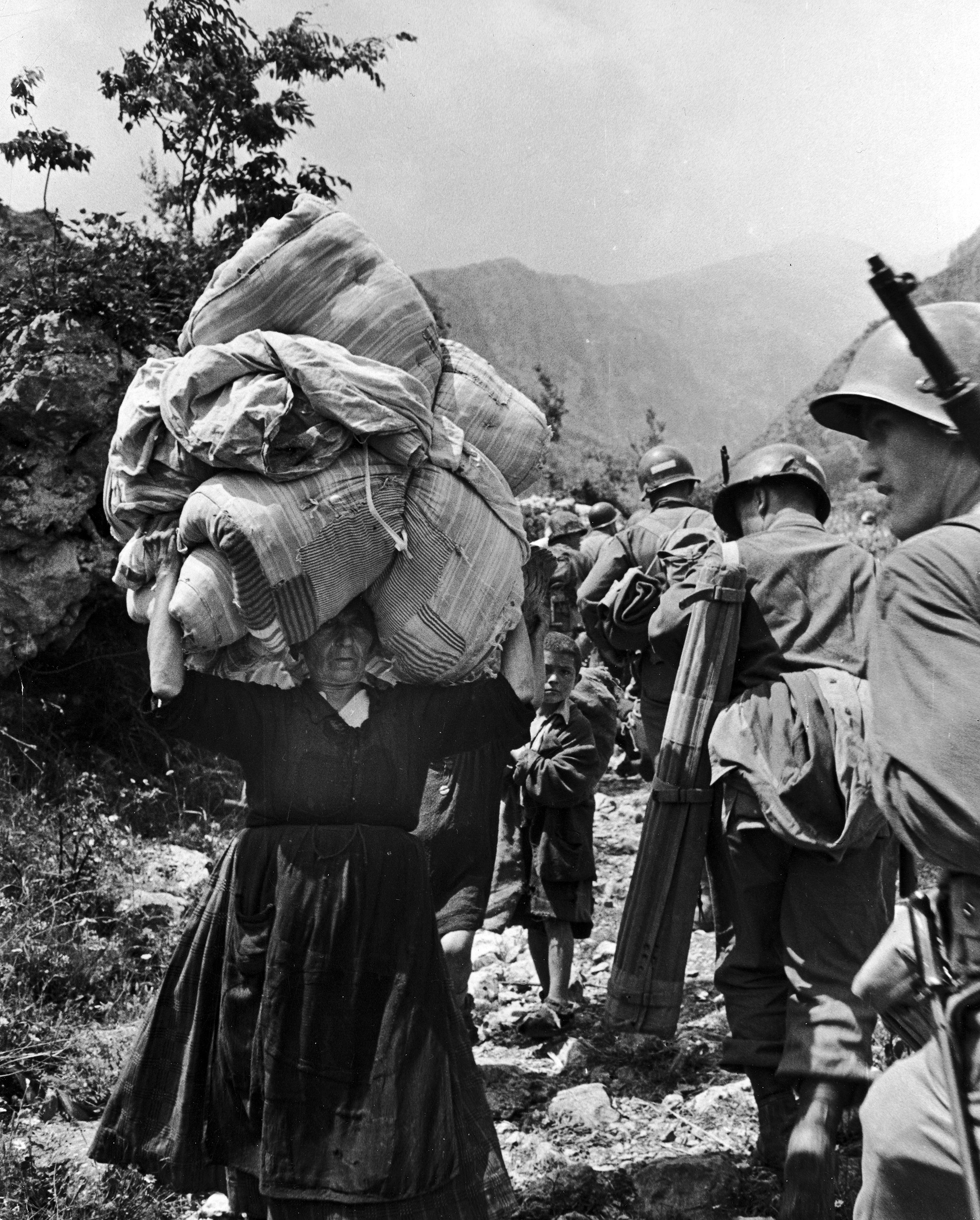 American soldiers passing refugees fleeing the fighting somewhere in the mountains of Italy during WWII. 1944.