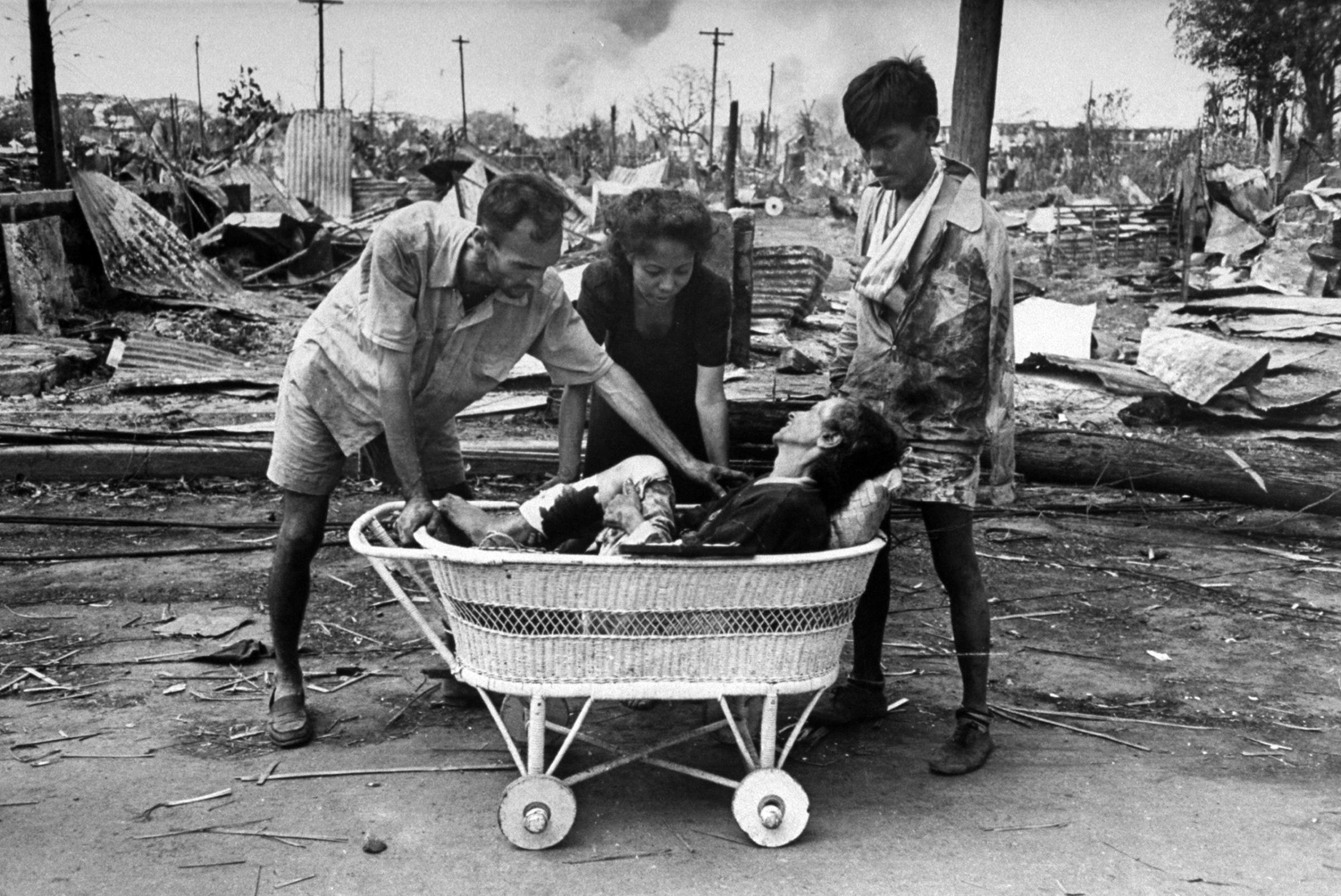 Friends using a baby carriage to transport a wounded woman to an aid station during the fight to reclaim the city from occupying Japanese troops. This image is an outtake from the March 5, 1945 photo essay: Santo Tomas is Delivered.
