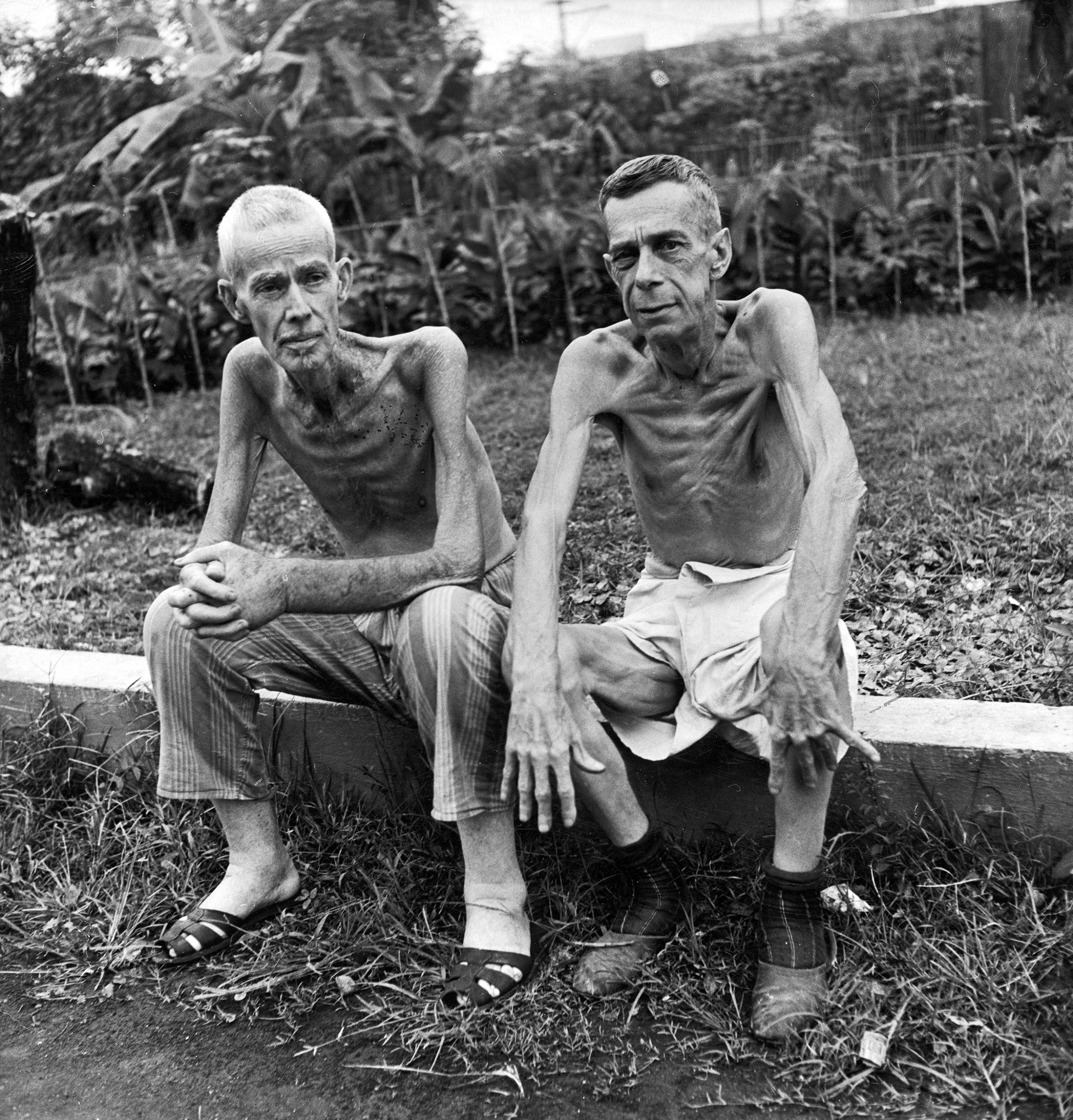 Two emaciated American civilians, Lee Rogers (L) John C. Todd, sitting outside a Japanese prison camp following their release by Allied forces liberating the city. This image appeared in the March 5, 1945 photo essay: Santo Tomas is Delivered.