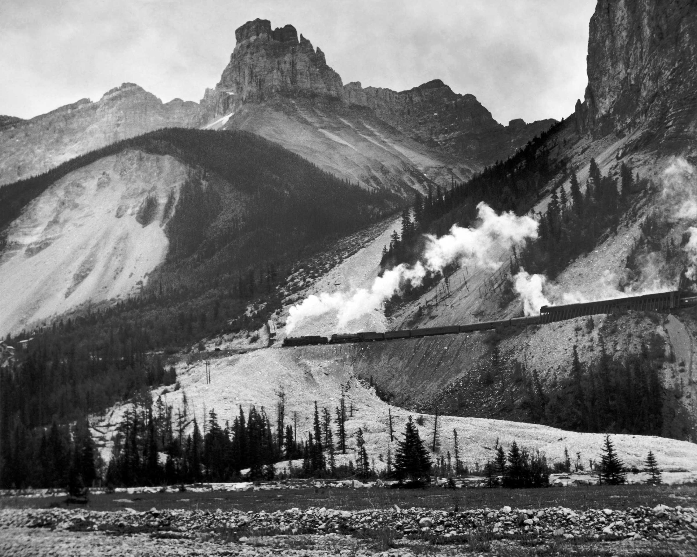 A freight train moves through the mountains of the President Range, Yoho National Park, British Columbia, Canada, 1951.