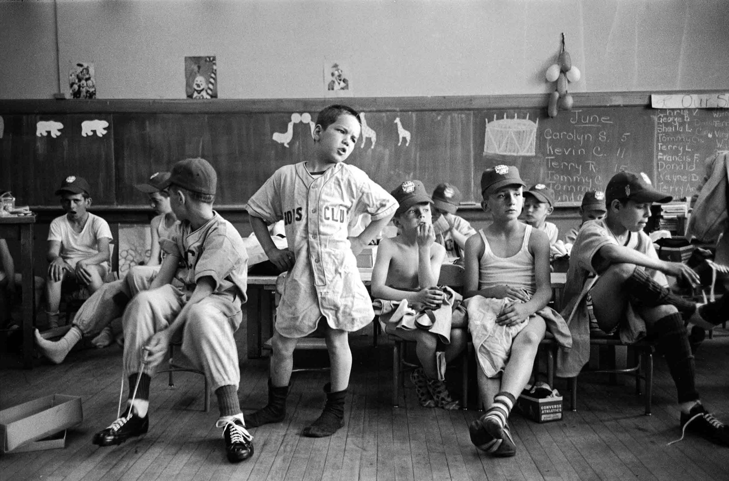 In a kindergarten classroom, baseball players try on new uniforms as Dick Williams (center) and others anxiously await missing parts of outfits, 1954.