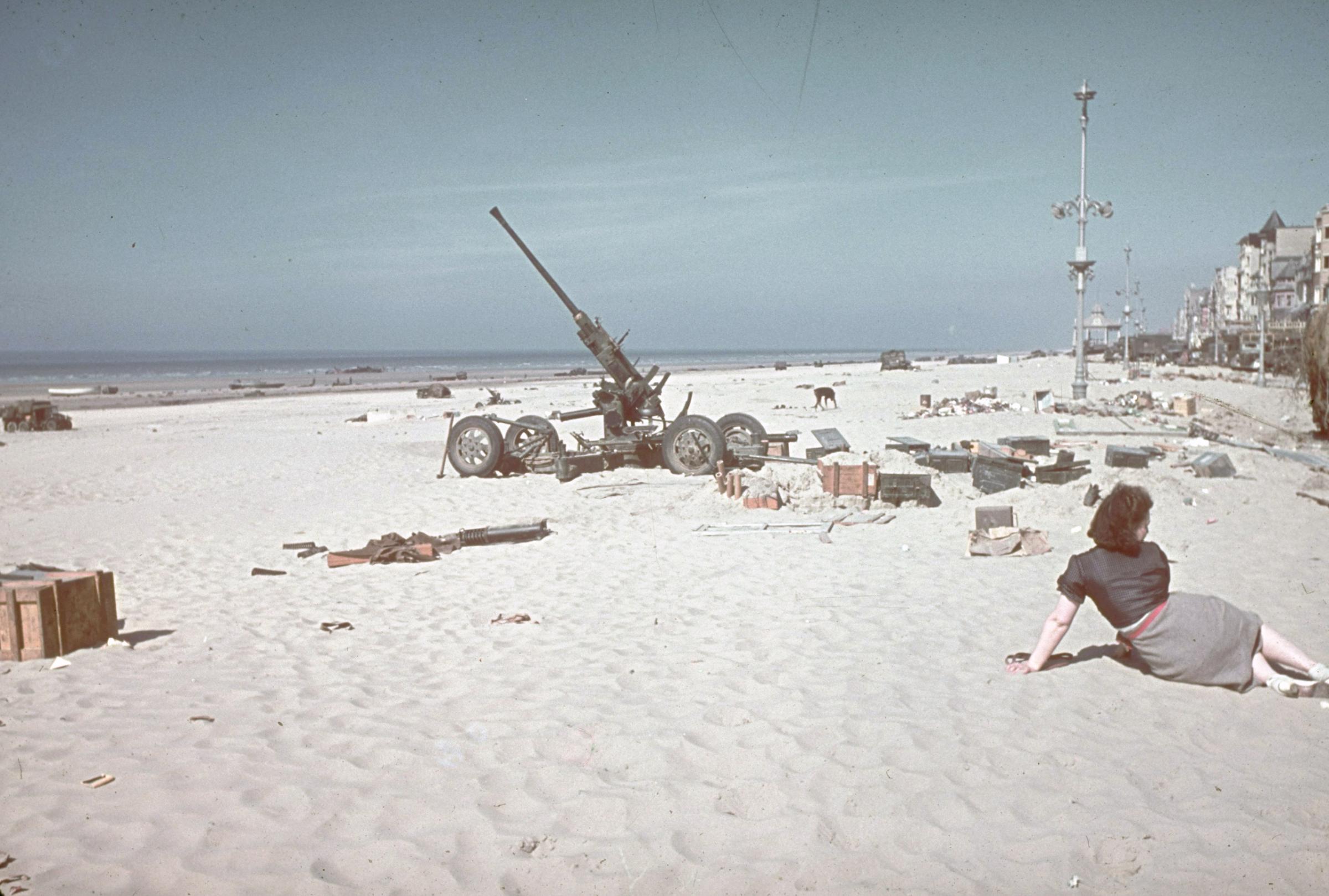 Woman lounging on beach strewn with abandoned supplies and a derelict artillery piece near Dunkirk after the Allied retreat. 1940.