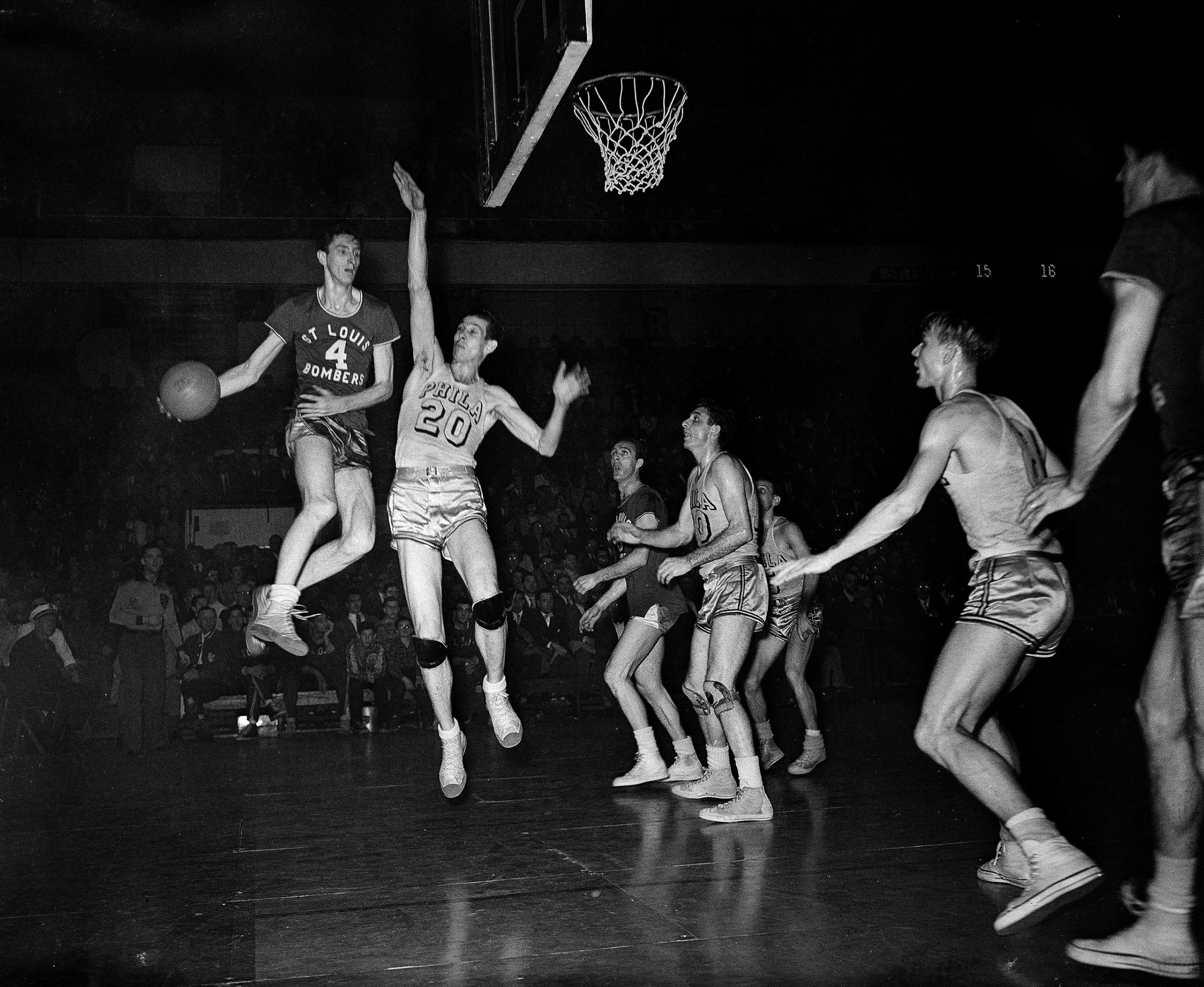 Red Rocha (4), St. Louis Bombers center, goes up in the air to make a pass in Basketball Association of America playoff game with the Philadelphia Warriors at the Arena, March 30, 1948. Chuck Halbert, lanky Warriors center, also leaves the floor in an attempt to block the pass.