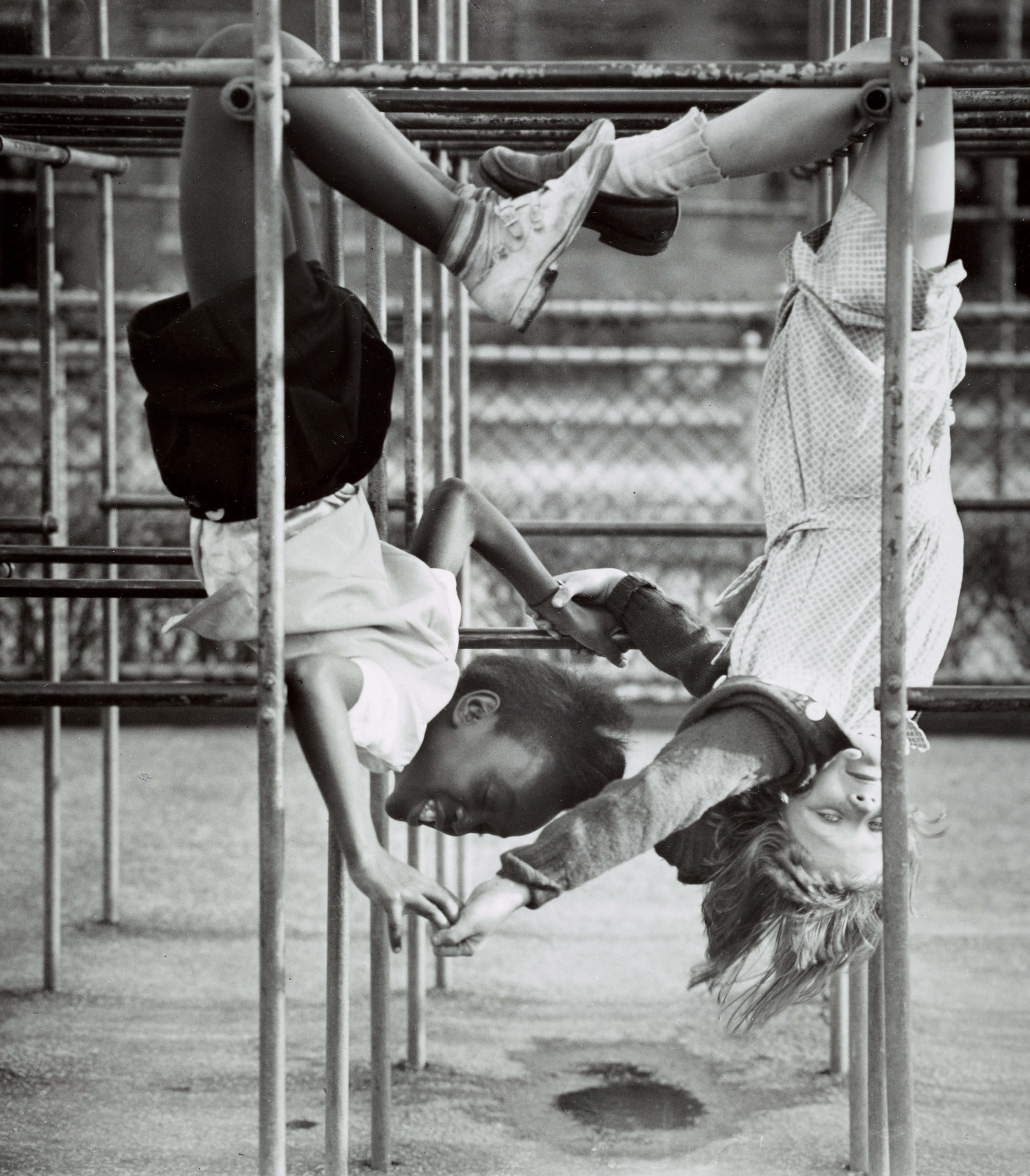 Two schoolgirls holding hands as they hang upside down from a jungle gym. Circa 1940s.