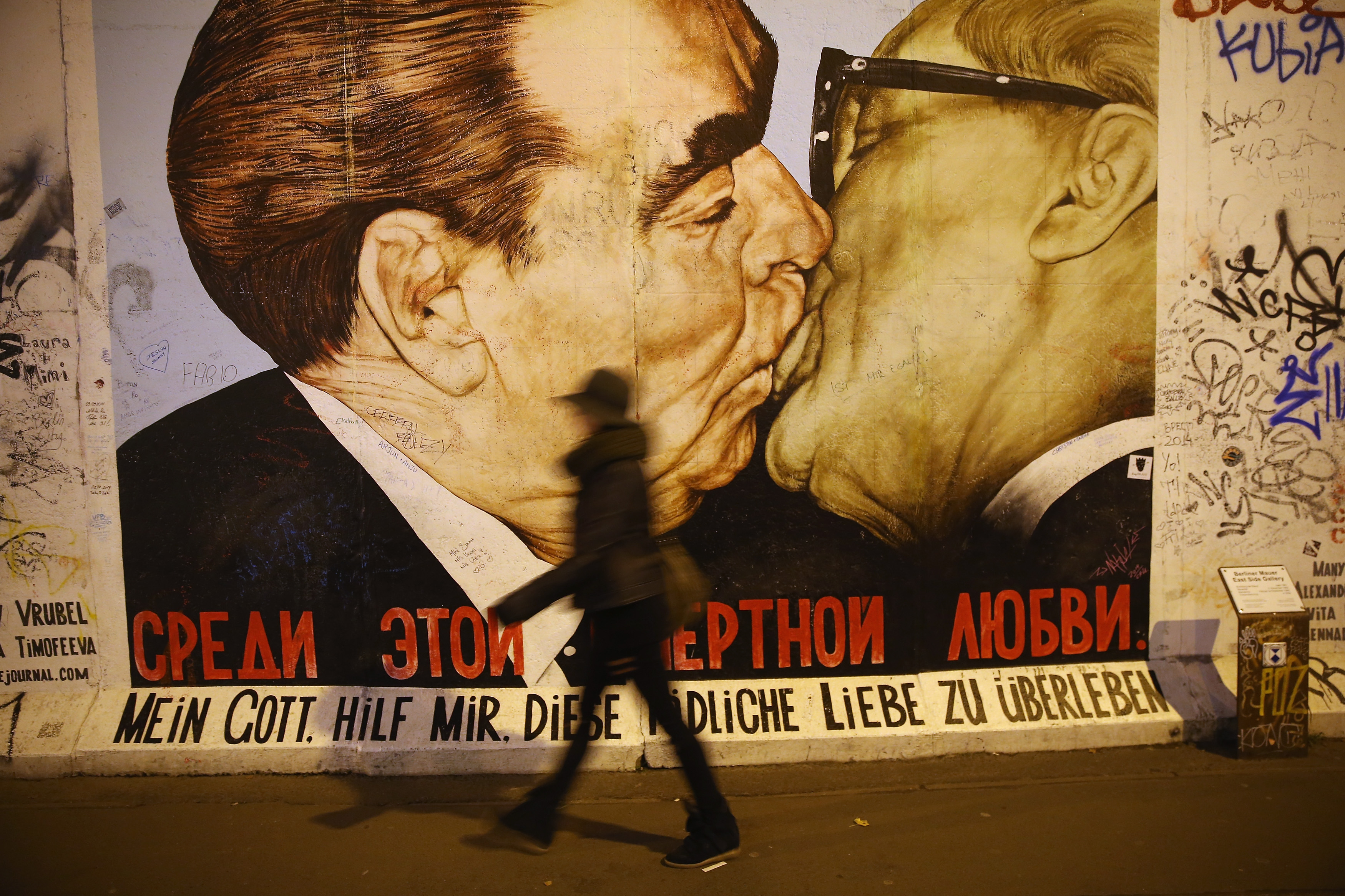 A visitor walks past a mural showing former Soviet leader Leonid Brezhnev (L) kissing former East German communist leader Erich Honecker by Russian painter Dmitri Vrubel at the East Side Gallery on Oct. 28, 2014 in Berlin, Germany. (Sean Gallup/Getty Images)