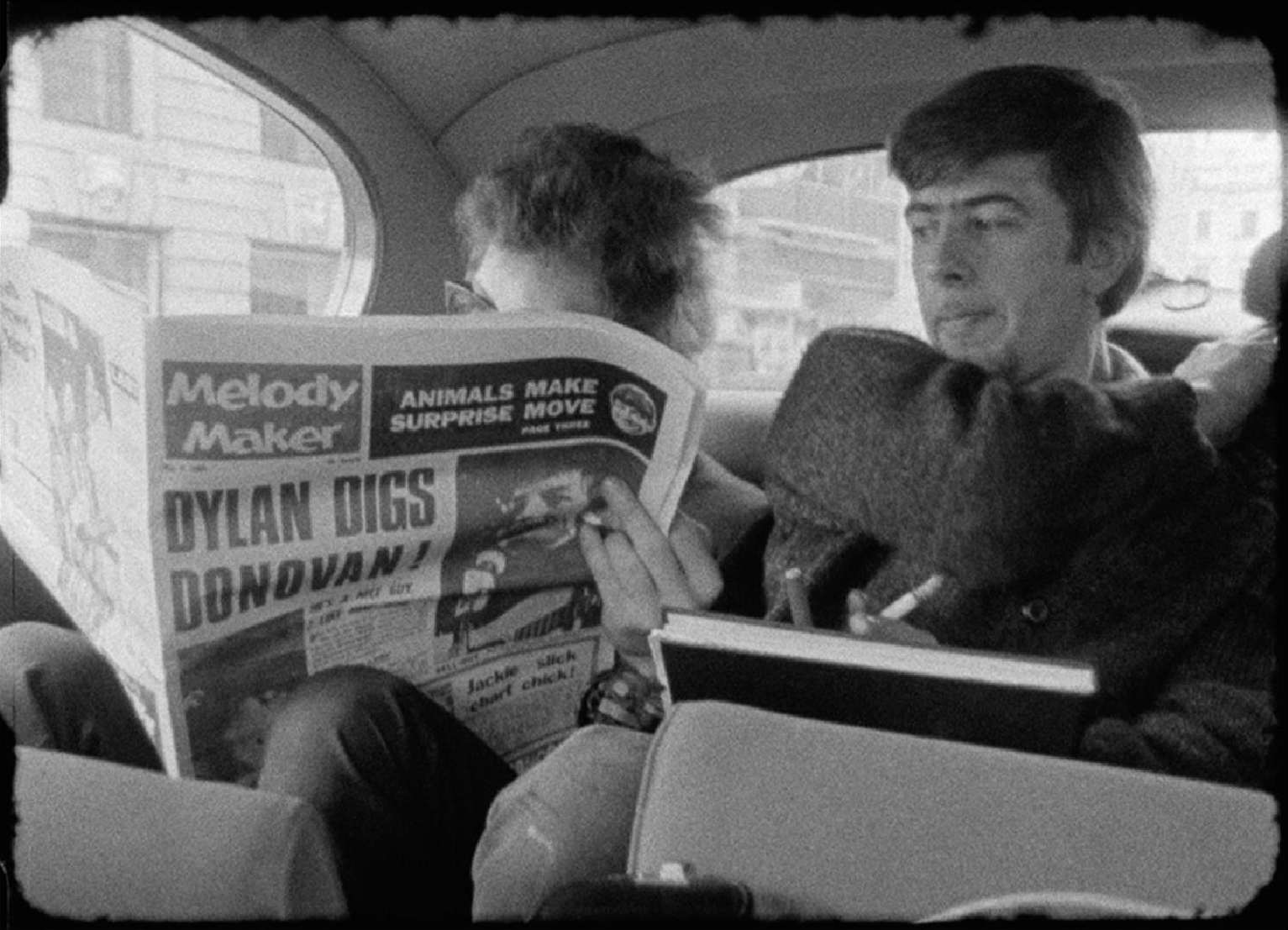 Bob Dylan reads Melody Maker, with John Mayall looking on, in London, 1965.