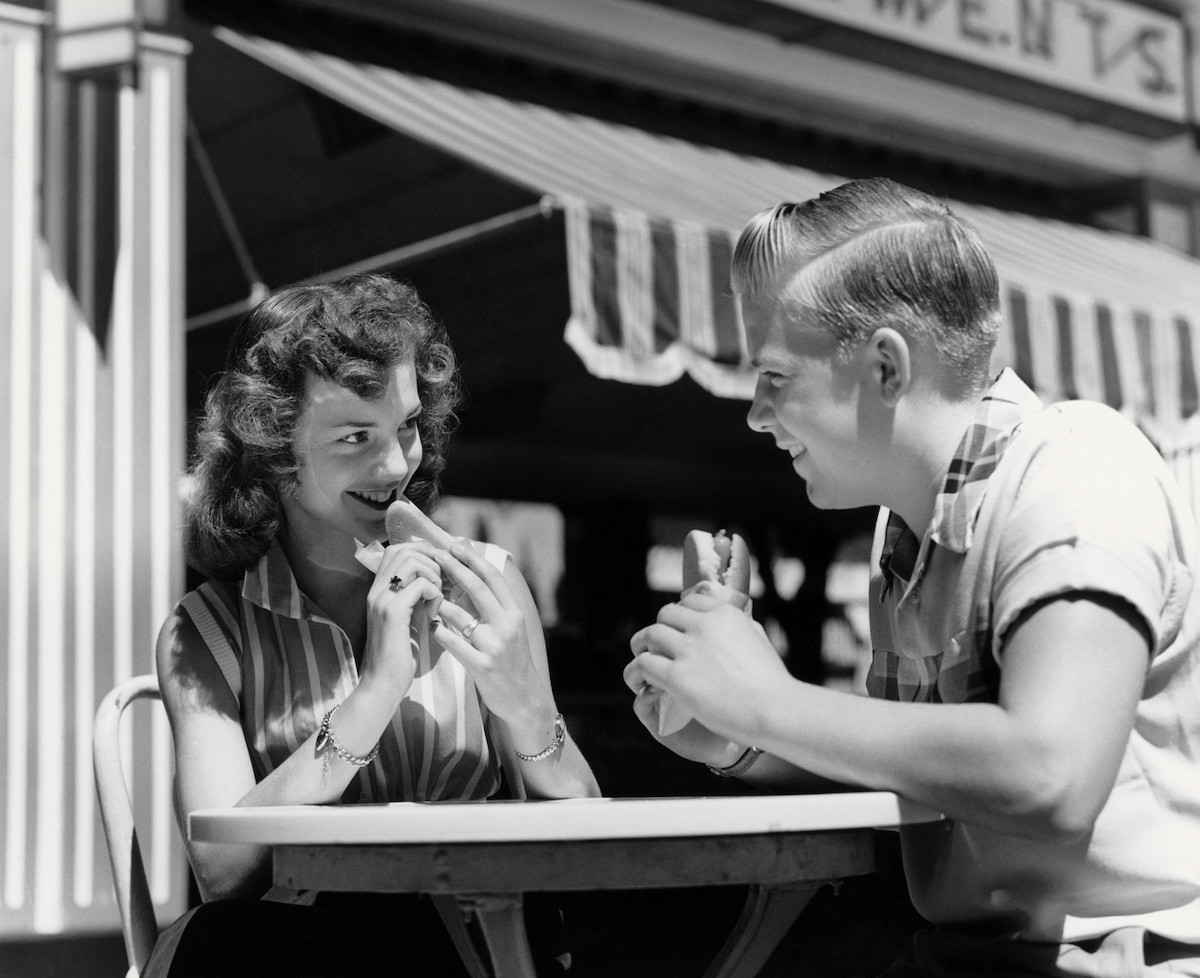 Teenage couple eating hotdogs outside at refreshment stand table, circa 1950 (H. Armstrong Roberts—Retrofile/Getty Images)