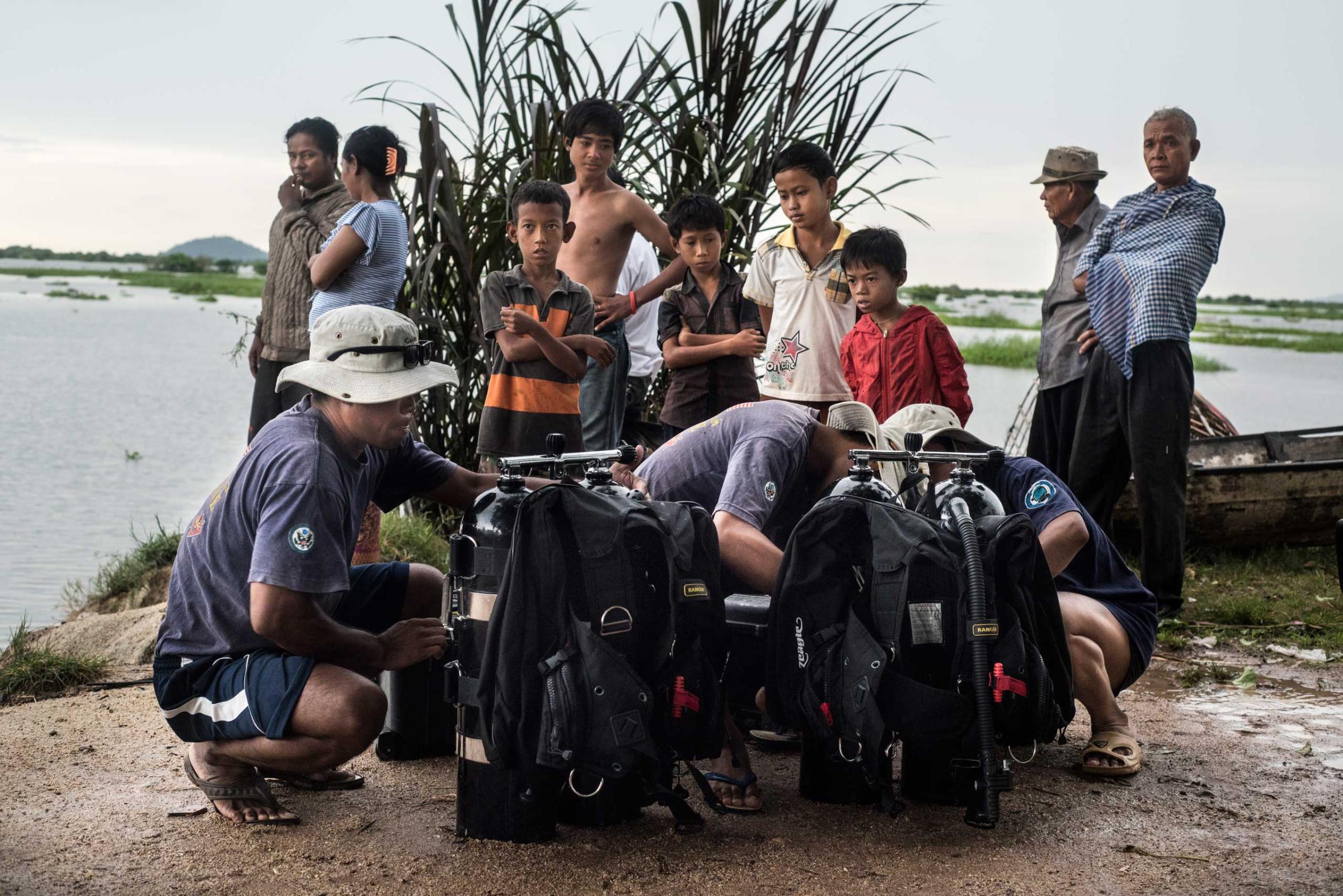 Members of the UXO salvage dive team prepare dive equipment on the banks of the Tonle Sap river overlooked by local villagers in Dec. 2014.