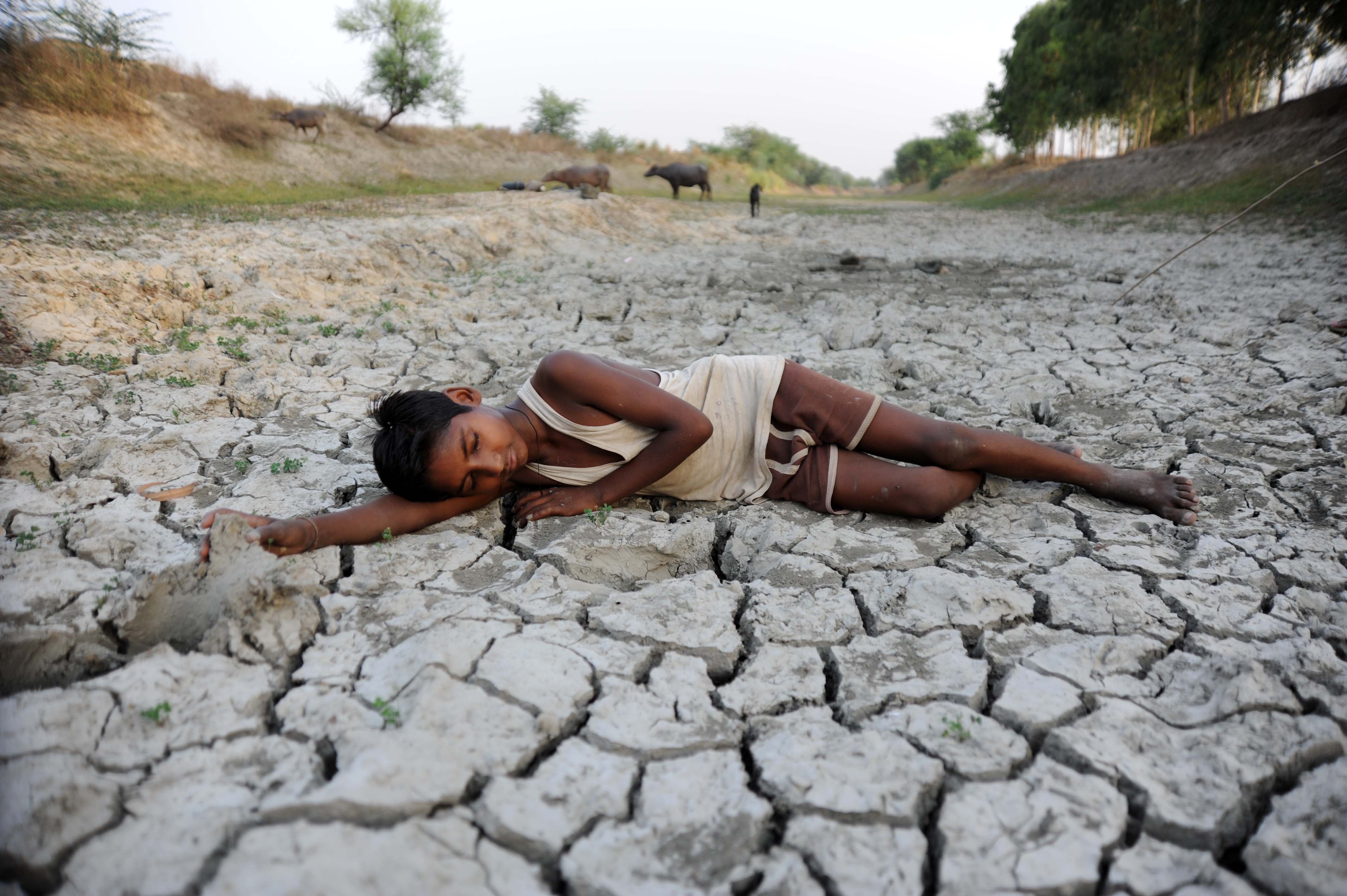 A child lies down on a dry bed of parched mud that is the